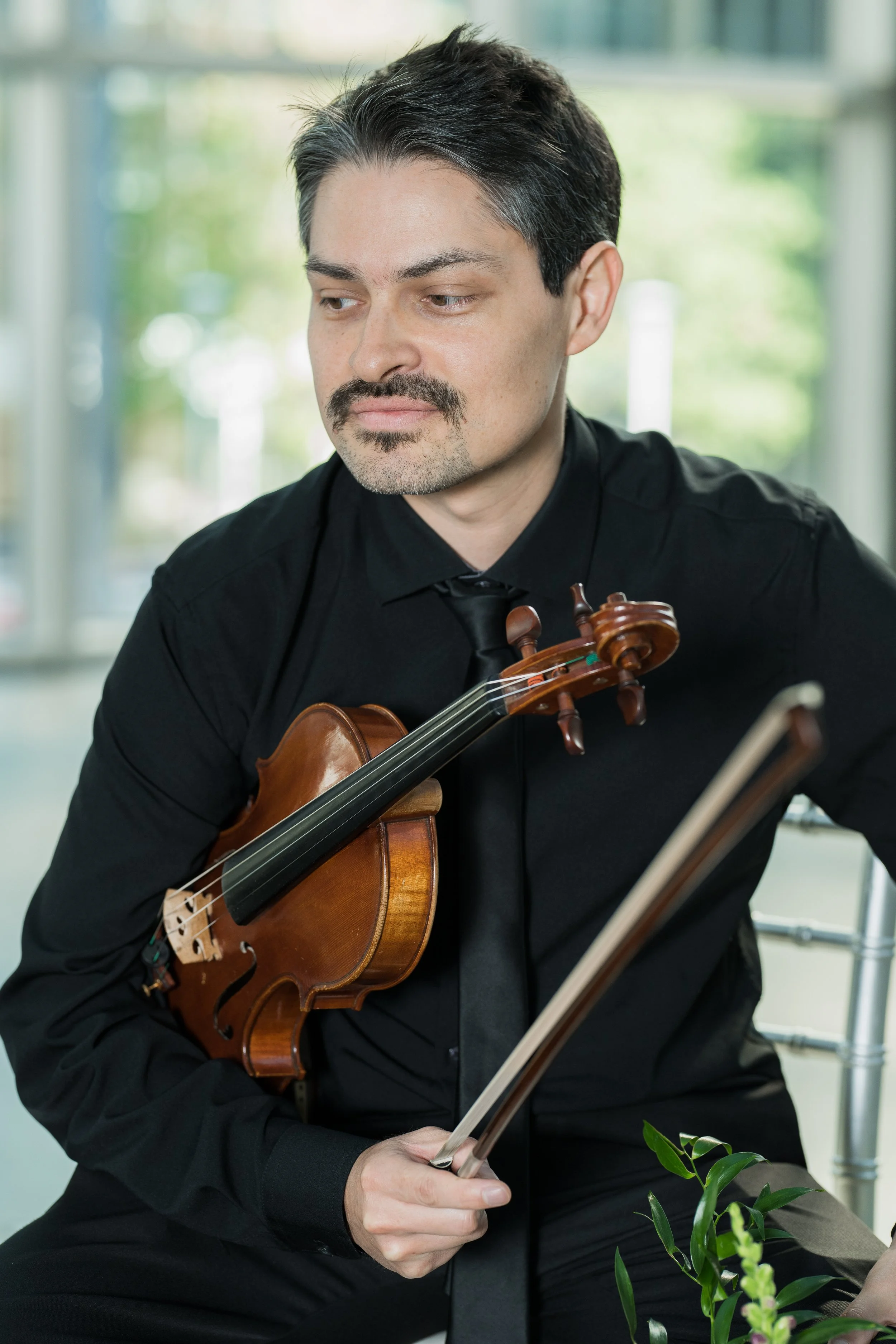 Hector Marchant holding his violin framed by a bright window.