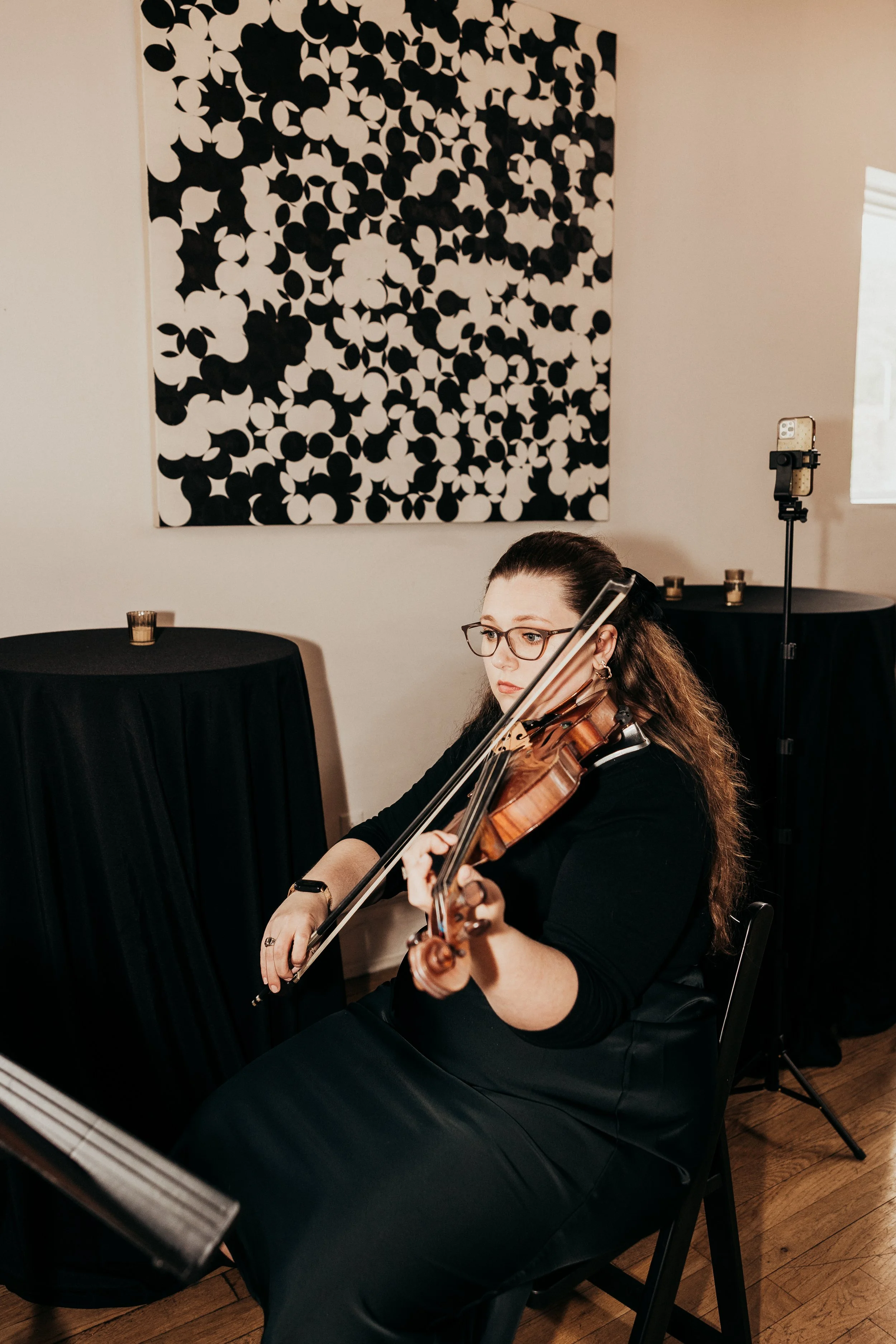Nicole Lennartz playing the violin in Bar Marco, with black and white abstract art on the wall behind her.