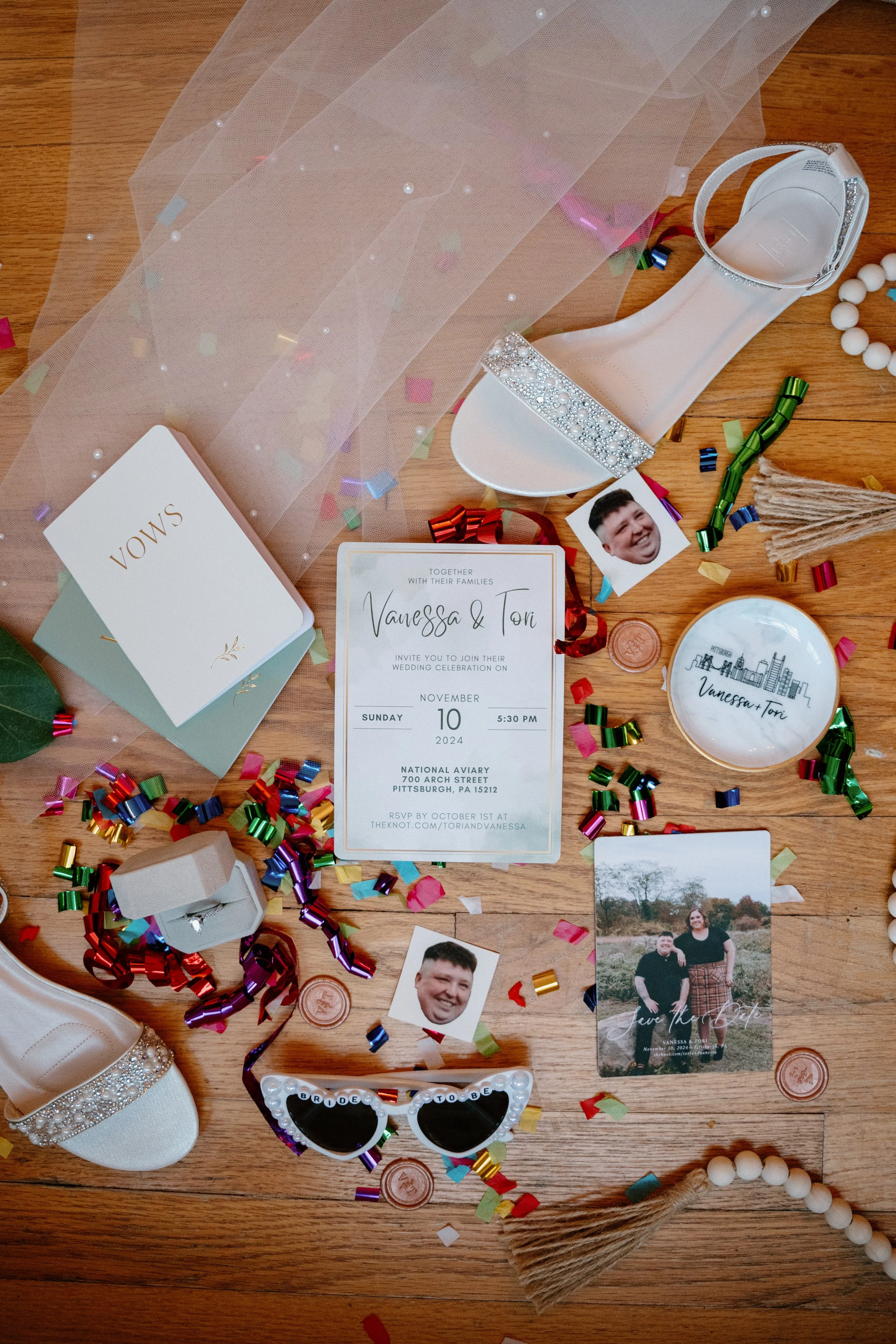 Wedding invitation, high heel shoes with rhinestones, vow cards, photographs, colorful confetti, and decorative items on a wooden floor.