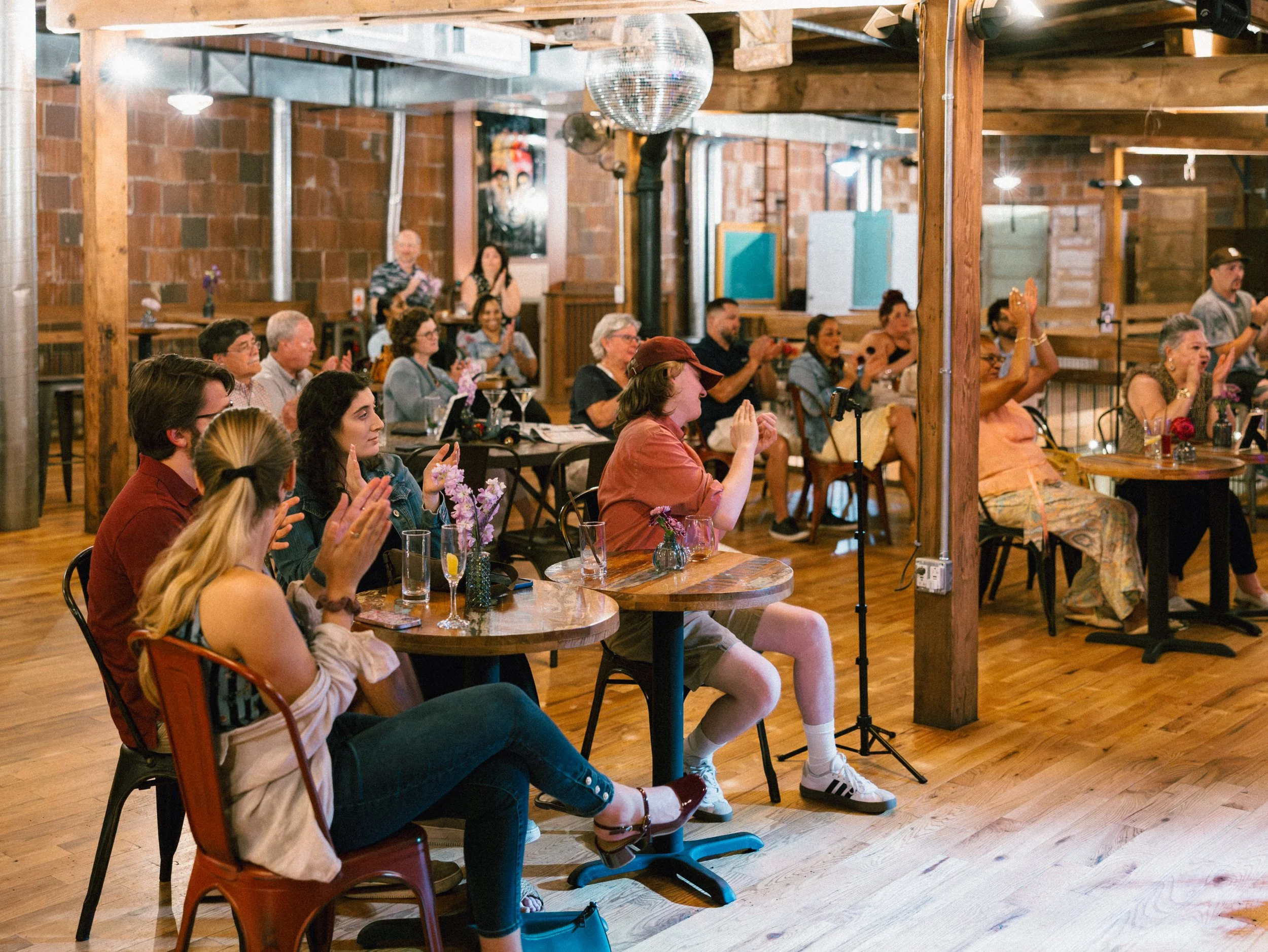 Group of people sitting at tables in a cozy, rustic venue with wooden beams, watching Radiant Strings.