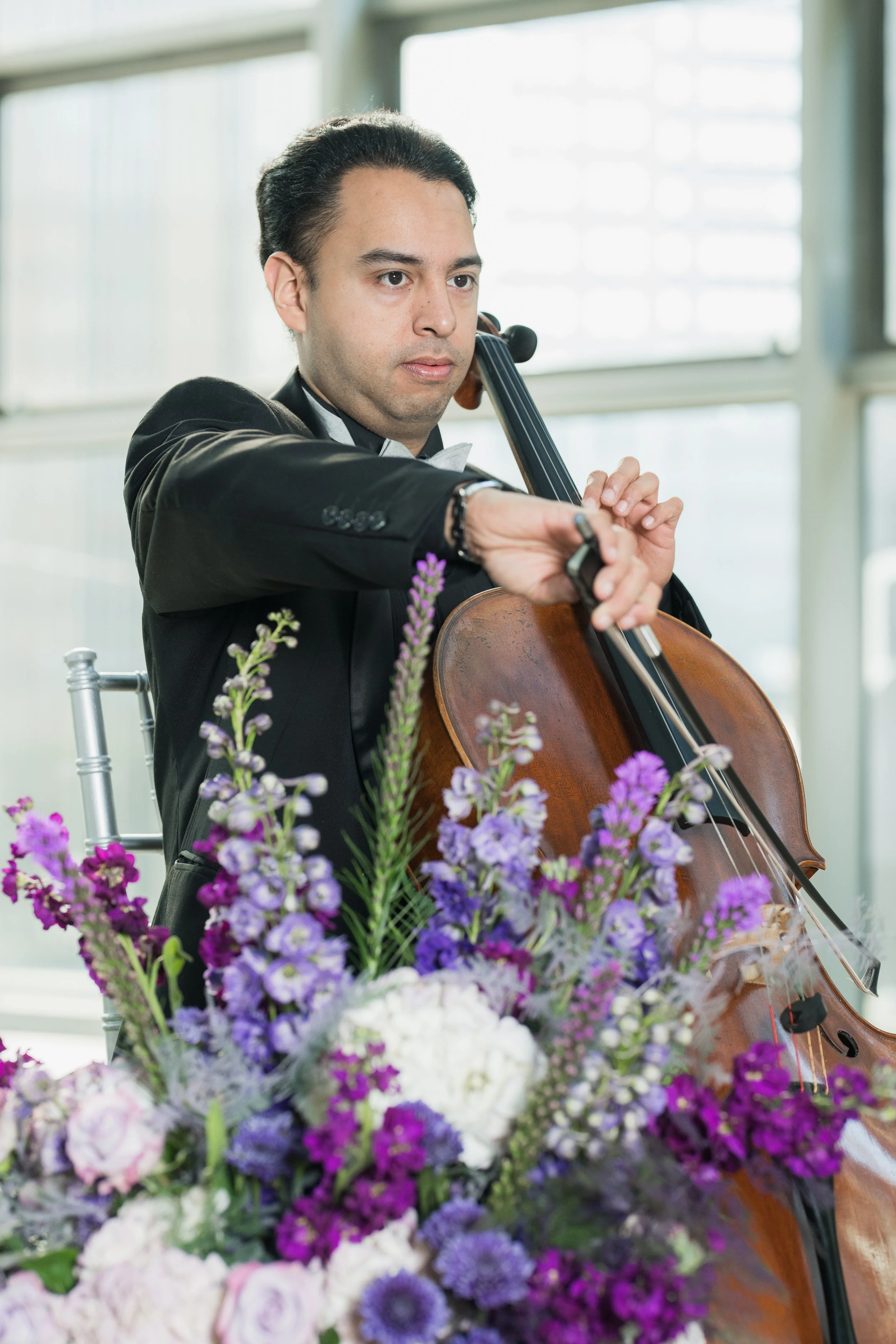 William Garcia playng the cello in front of a purple flower arrangment.