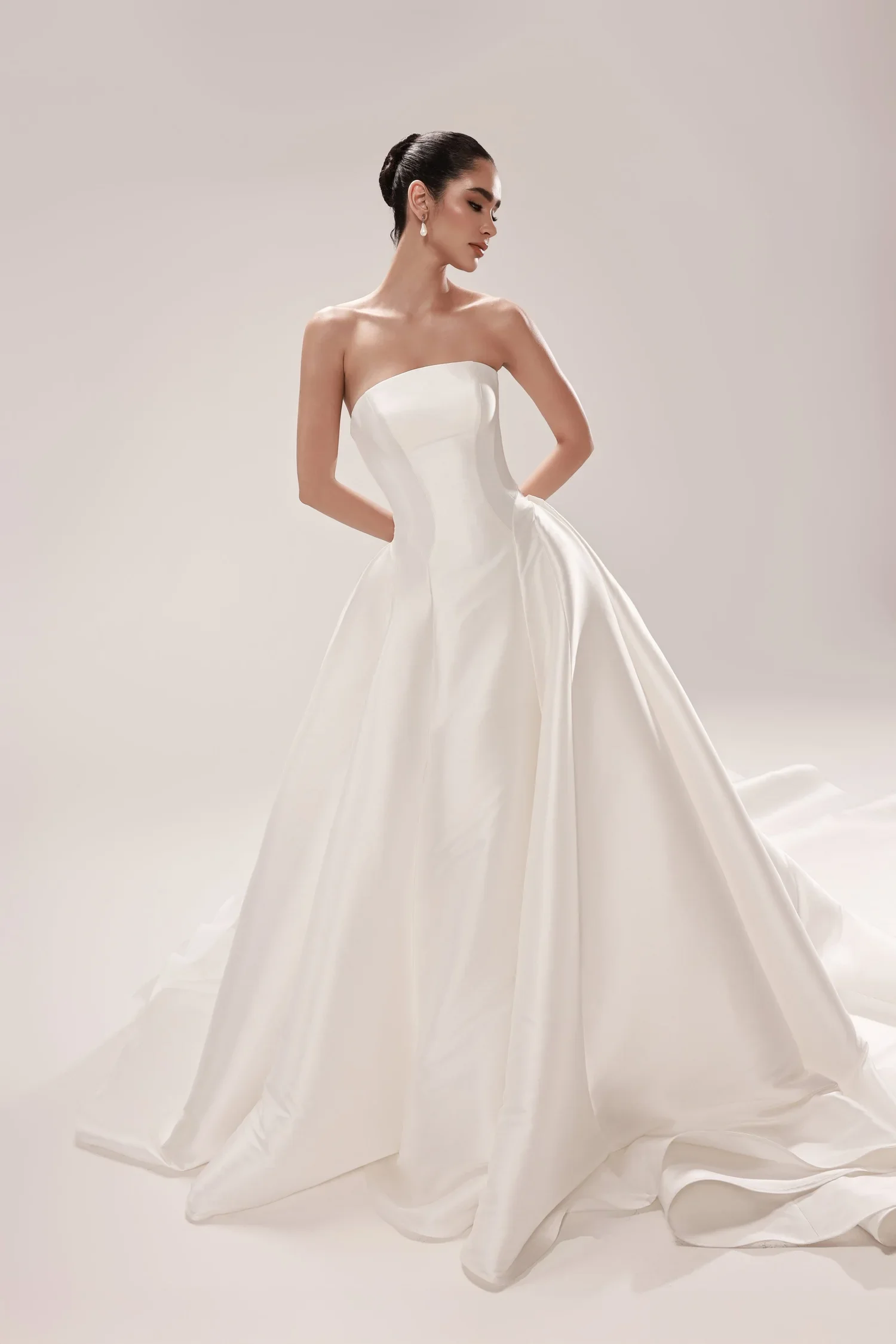 A woman in a strapless white wedding dress with a full skirt poses against a plain background.