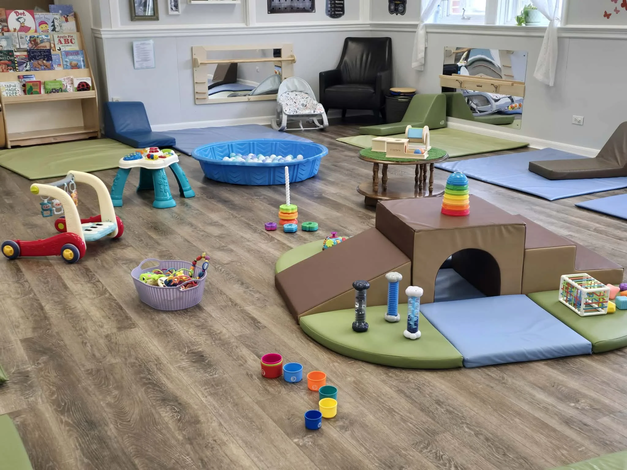 A children's playroom with soft mats, toys, and a ball pit, featuring various colorful play equipment and books.