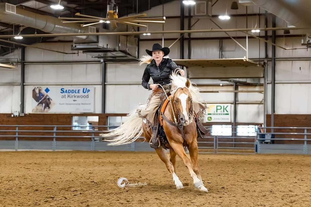 A woman riding a horse inside an indoor riding arena.