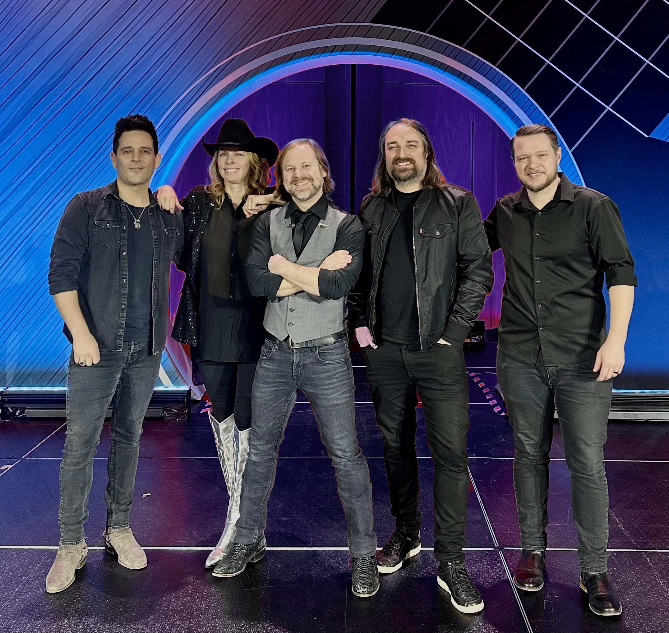 Five people standing together in front of a colorful, futuristic background with curved lines and glowing lights. They are smiling and dressed casually, with some wearing jackets or shirts, and one woman wearing a black cowboy hat.