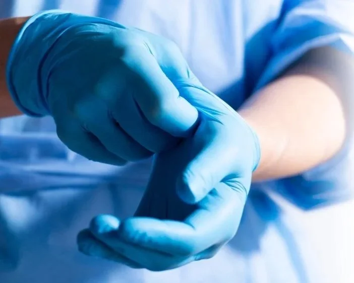 A healthcare professional wearing blue gloves adjusting or putting on gloves