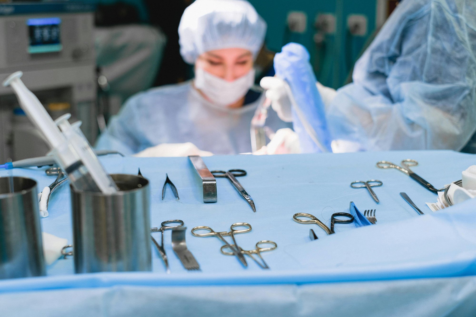 A surgeon in an operating room wearing a surgical mask, cap, and gown, preparing surgical tools on a blue sterile cloth during surgery.
