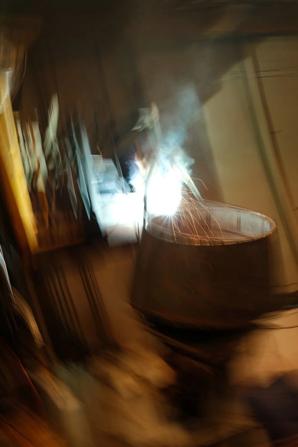 Heavy Fabrication Services. Welding in progress with sparks flying, creating bright light and smoke inside a workshop or industrial setting.