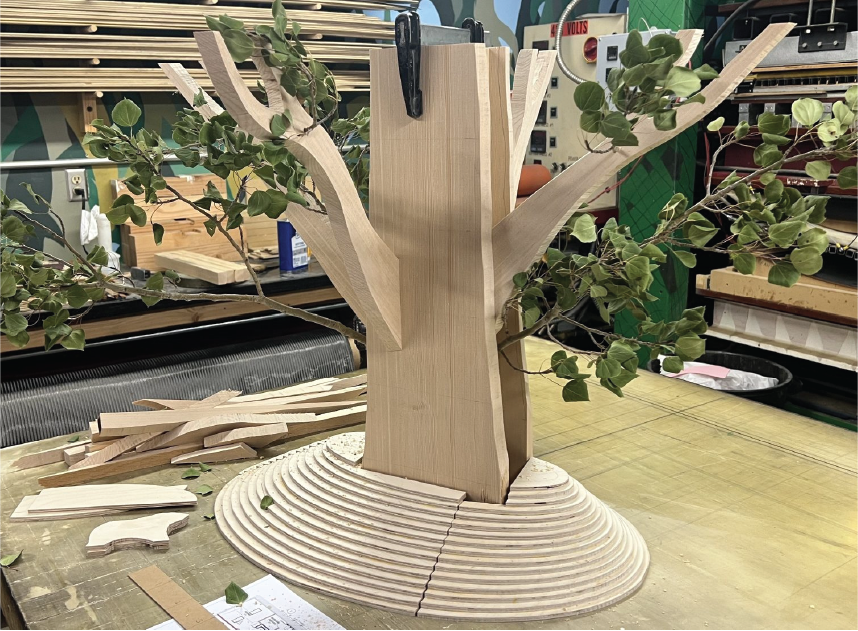 Wooden tree sculpture with leafy branches on a worktable.