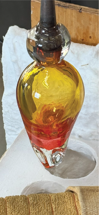A multicolored glass ornament with a black top, featuring yellow, red, and orange hues, placed on a white surface.