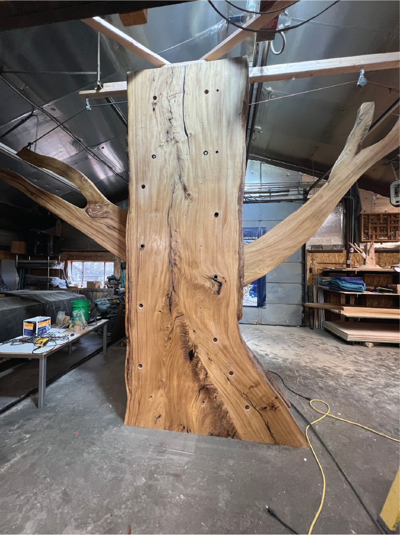 A large wooden slab with natural edges and visible wood grain, mounted vertically in a woodworking or carpentry workshop.