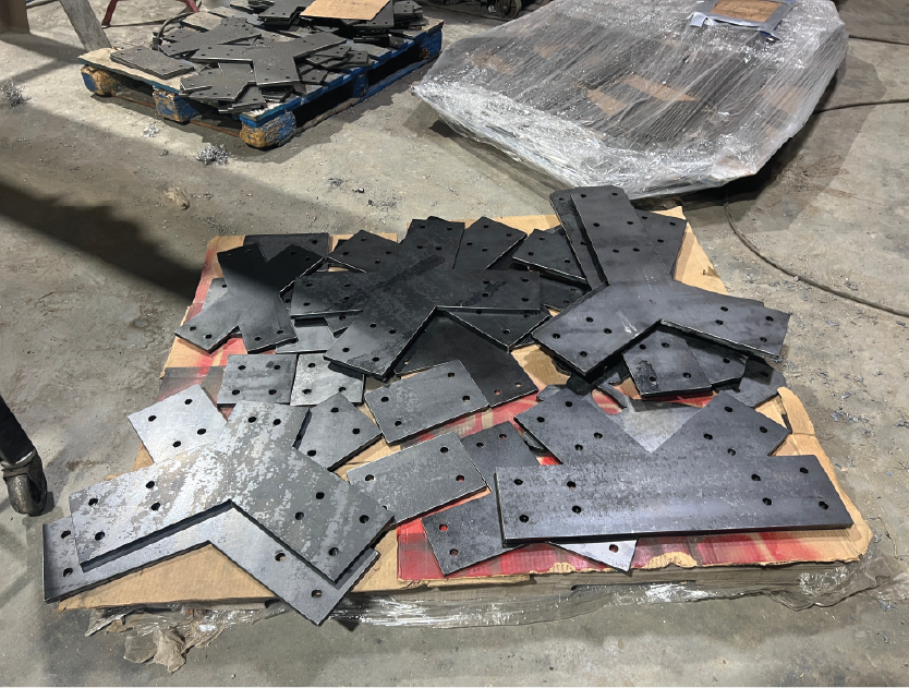 Metal parts with holes scattered on a wooden surface in a workshop.