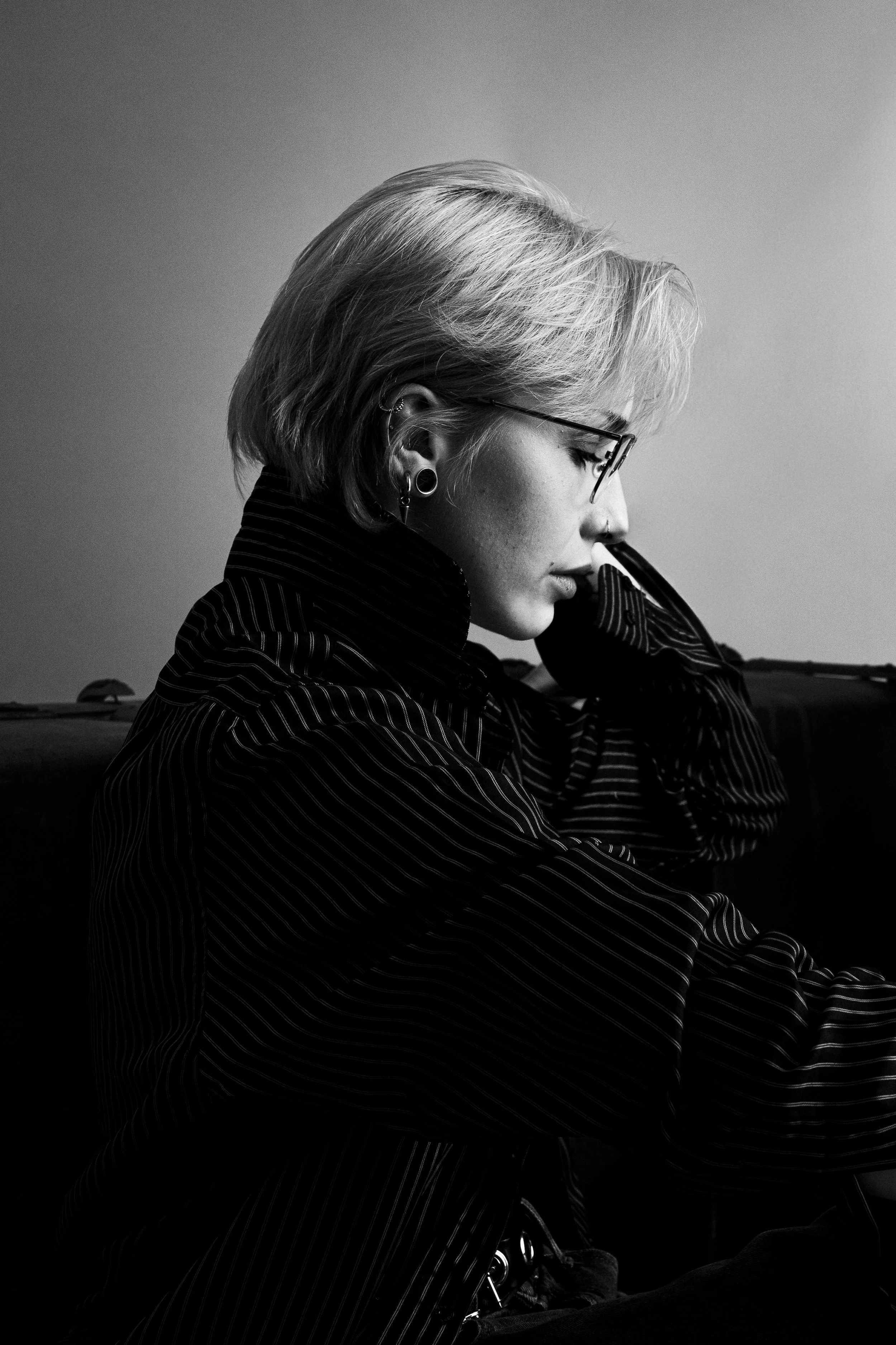 Schwarz-weiß Portrait einer jungen Frau mit kurz geschnittenem Haar, die eine Brille trägt und nachdenklich ist.