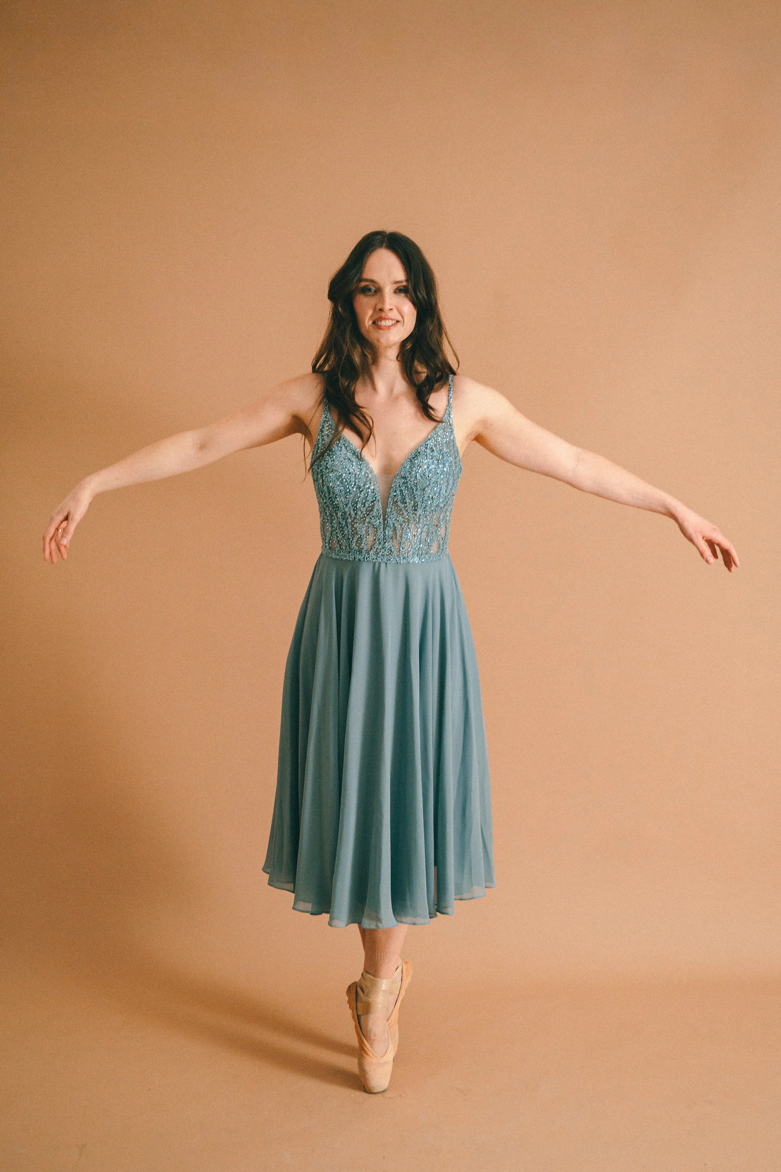 Tänzerin in blauem Abendkleid auf Spitze tänzelt auf Spitze Ballettschuhen auf beigem Hintergrund.