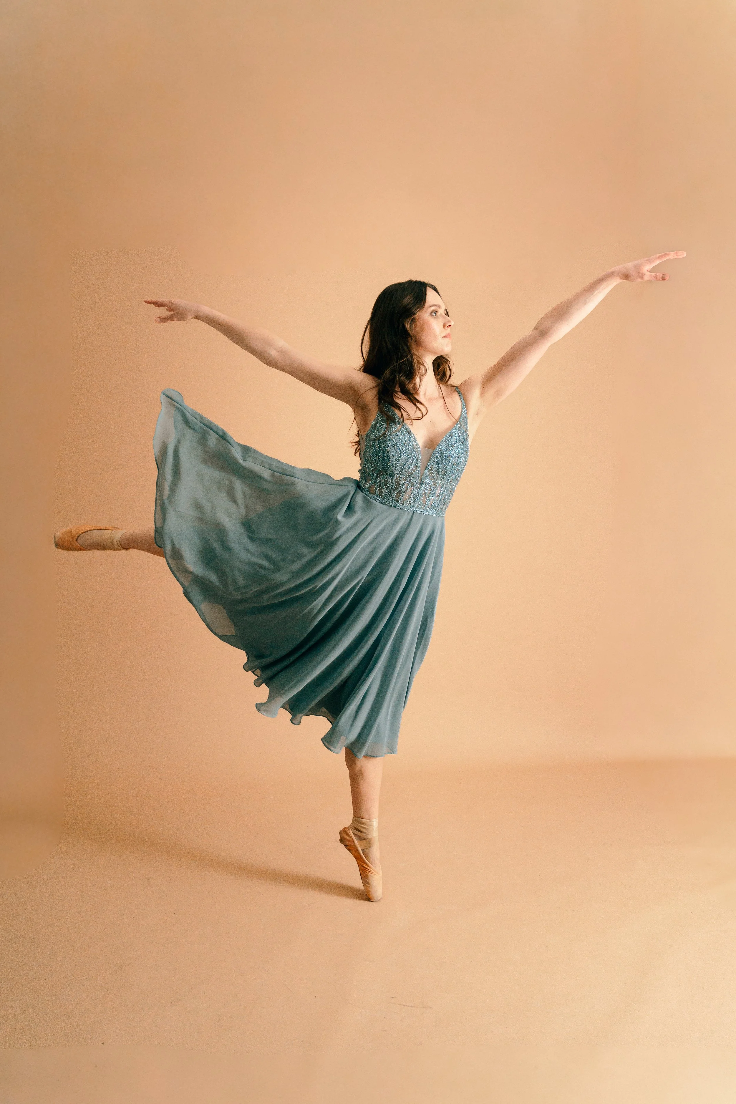 Balletttänzerin in einem blauen Kleid, die auf Pointen tanzt gegen einen hellen, einfarbigen Hintergrund.