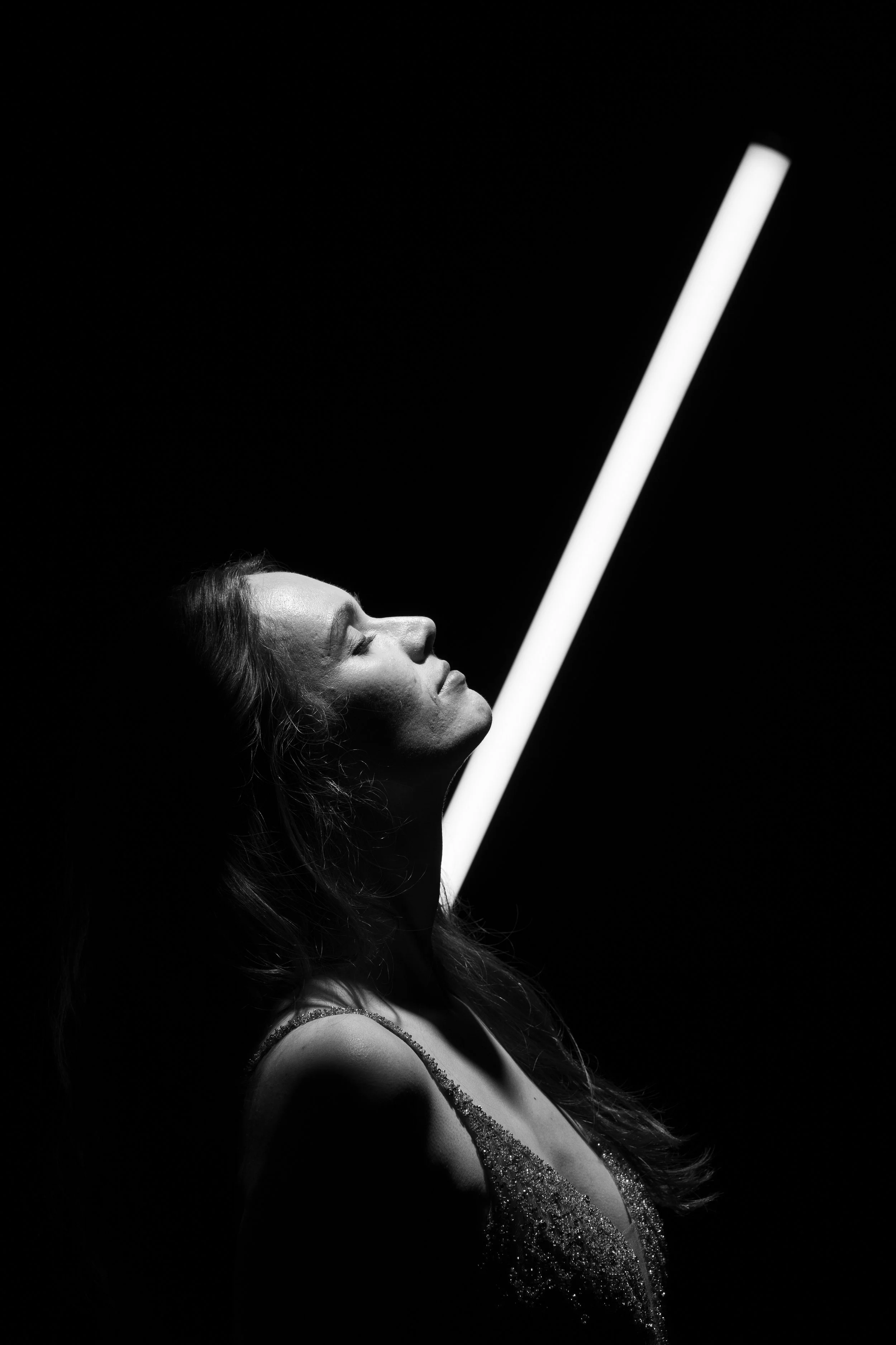 Schwarze und weiße Nahaufnahme einer Frau mit geschlossenen Augen, die einen hellen vertikalen Lichtstab hält.