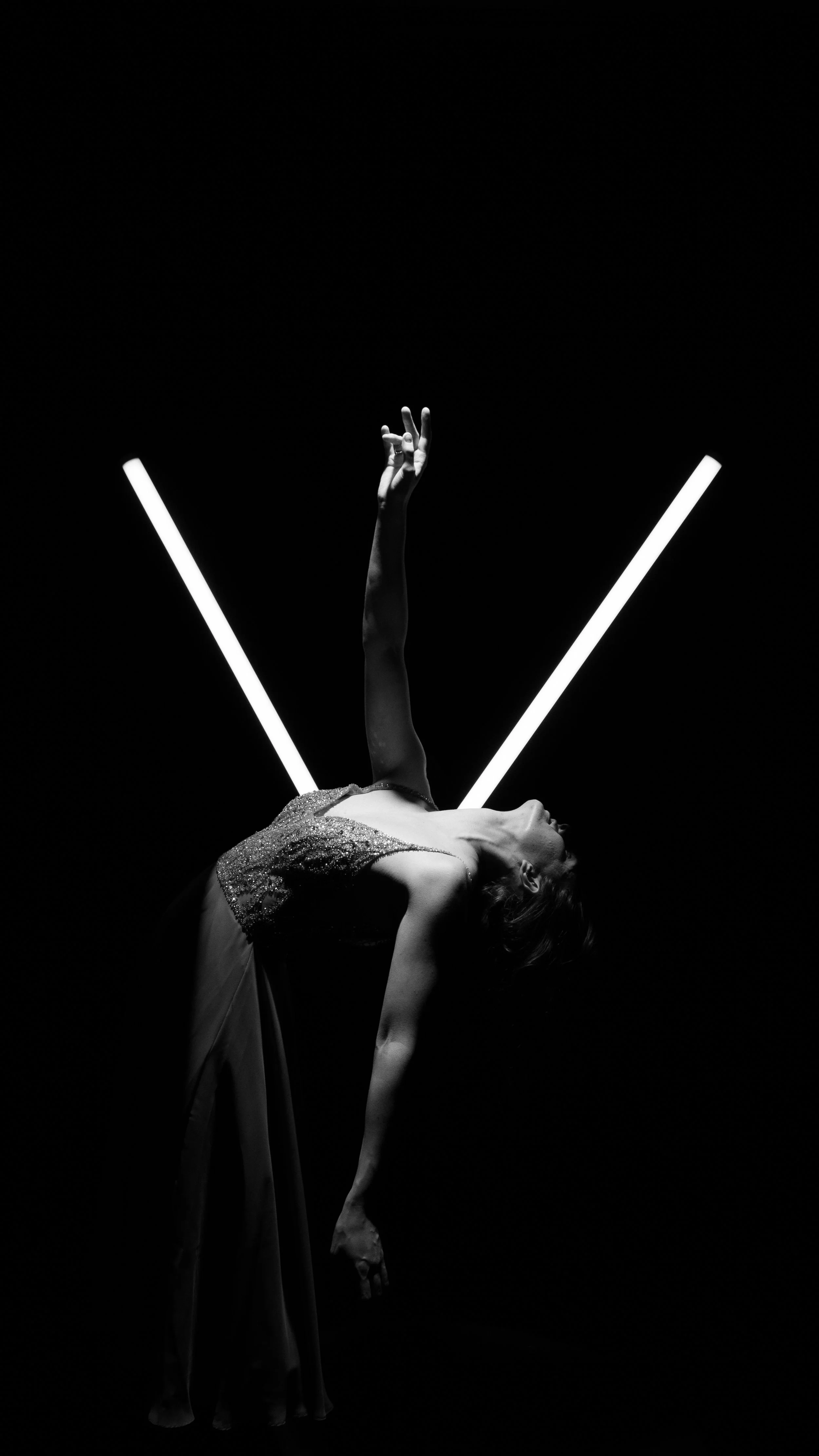 Schwarz-Weiß-Foto einer tanzenden Frau in eleganter Kleidung, die in Anlehnung an eine künstlerische Pose geformt ist, mit zwei leuchtenden Linien im Hintergrund.