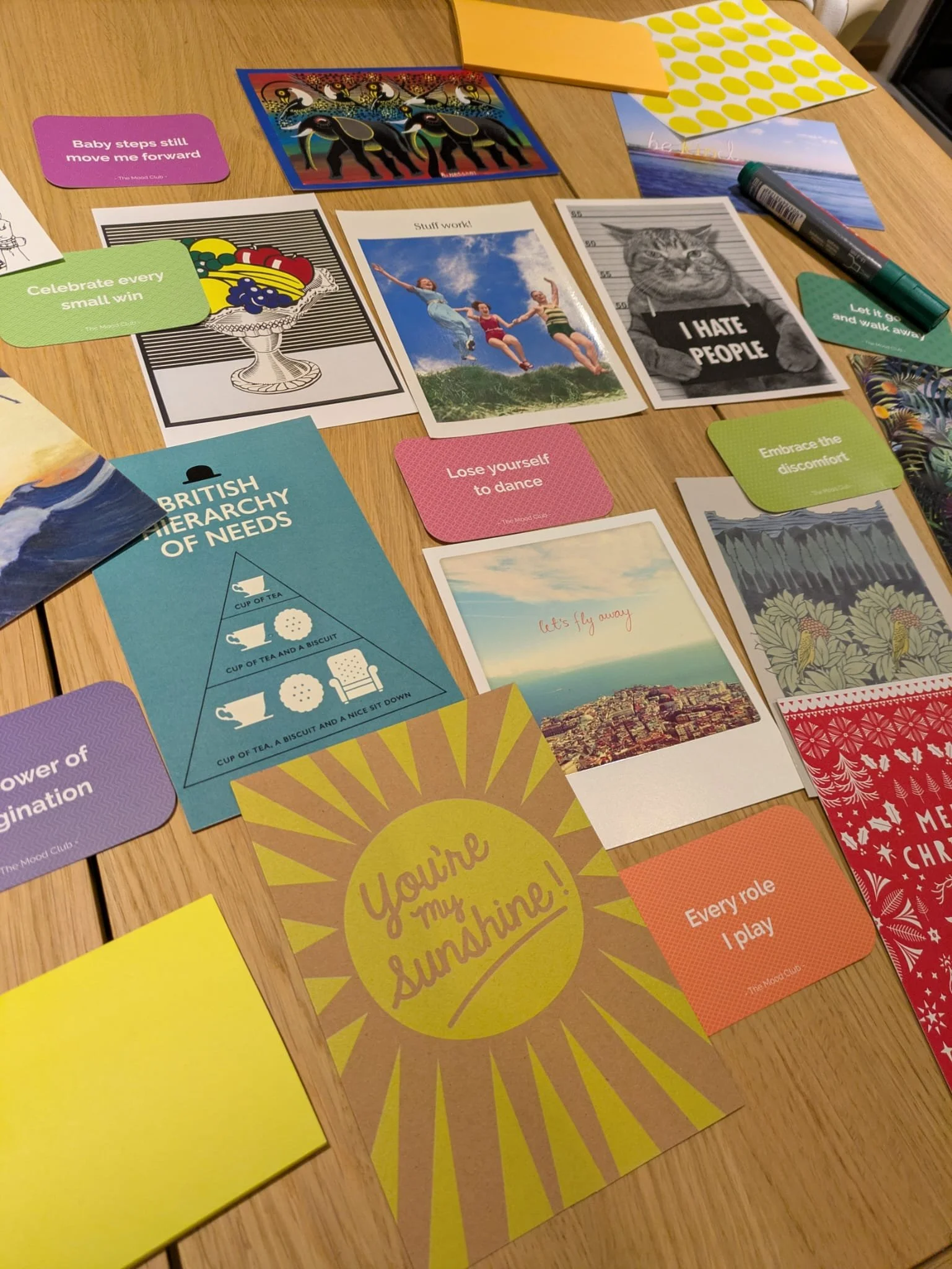 A collage of colorful cards and papers with motivational and humorous messages, images, and illustrations spread across a wooden table.