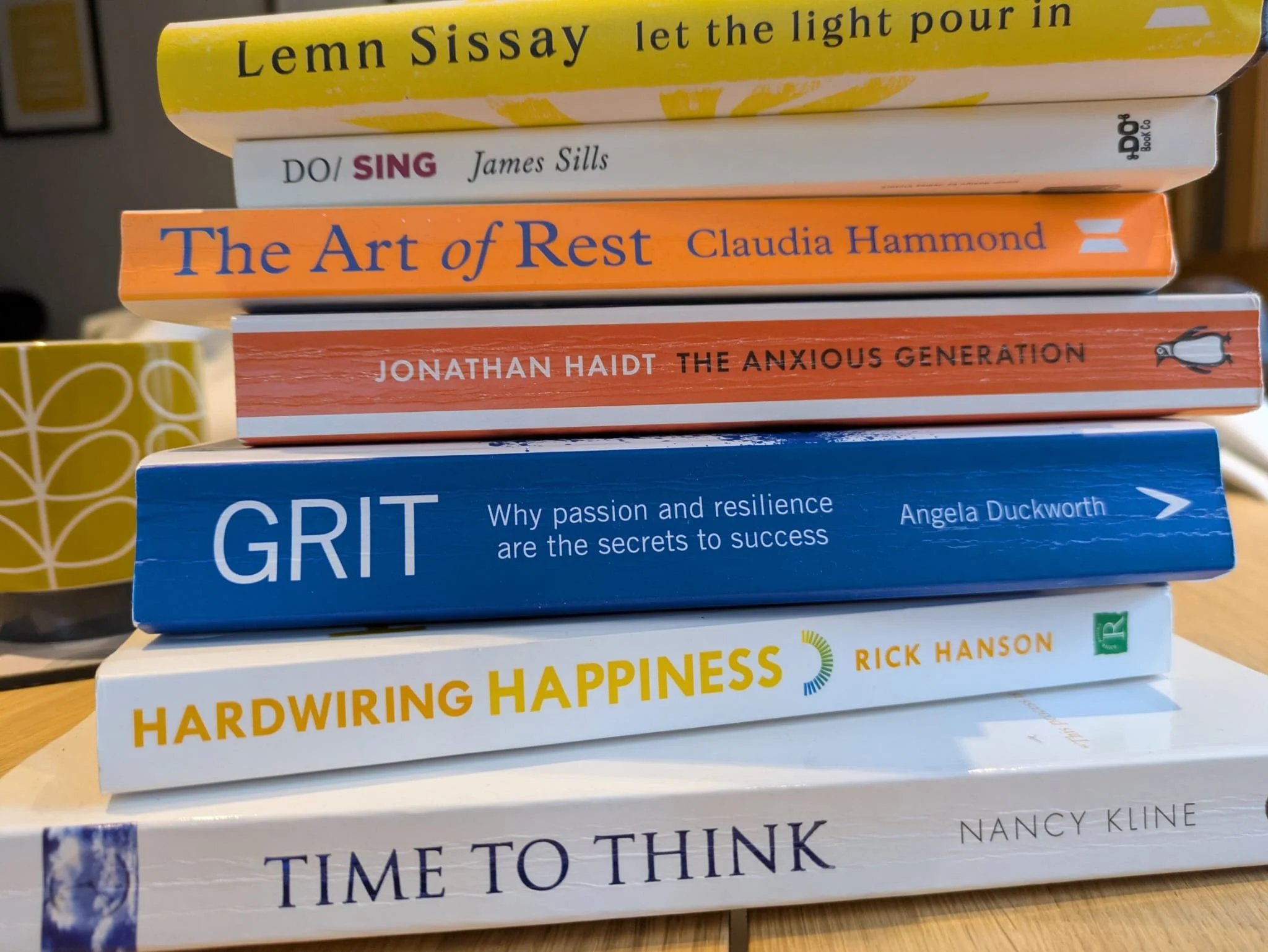 Stack of eight books on a table, with titles including "Lemn Sissay let the light pour in," "Do/Sing" by James Sills, "The Art of Rest" by Claudia Hammond, "The Anxious Generation" by Jonathan Haidt, "Grit" by Angela Duckworth, "Hardwiring Happiness" by Rick Hanson, and "Time to Think" by Nancy Kline.