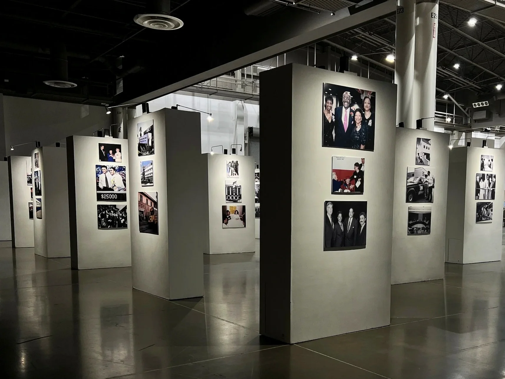 An art exhibition with photo panels displayed on white partitions inside a gallery space.