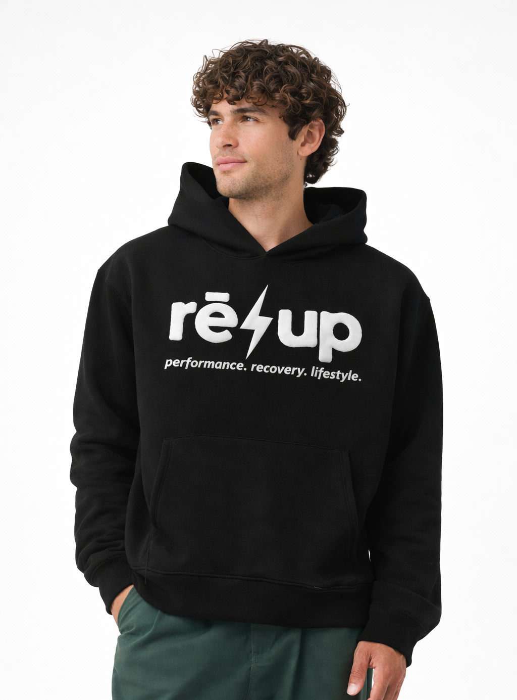 Young man with curly hair wearing a black hoodie with 'réup' and a lightning bolt logo, standing against a white background.