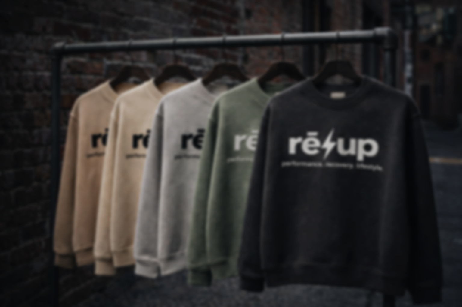 Five sweatshirts hanging on a clothing rack, each with the text "reup" and the tagline "performance. recovery. lifestyle." printed on them, set against a dark urban background.