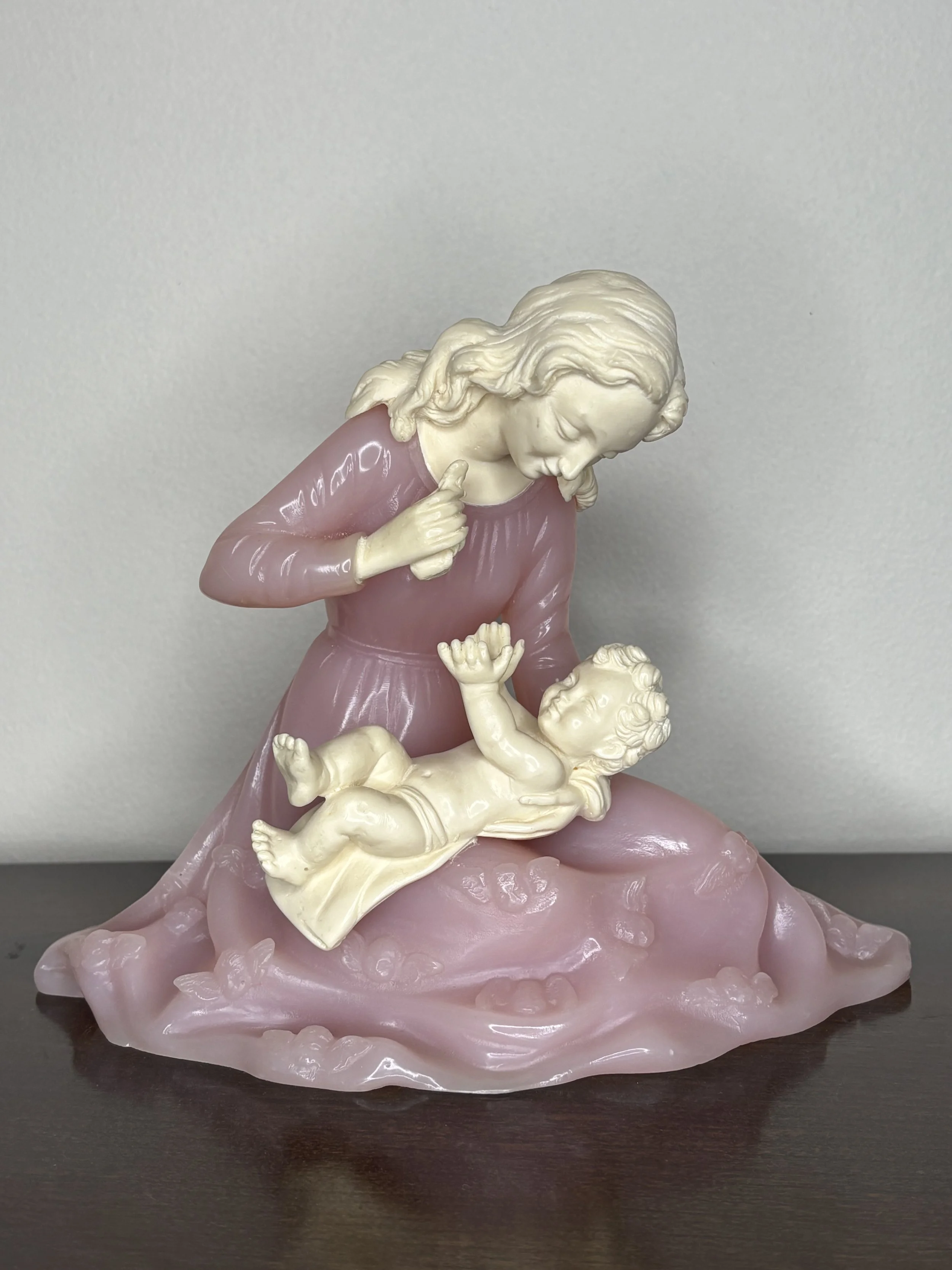 Decorative sculpture of Mother and baby Jesus with pink and cream colors on a dark surface