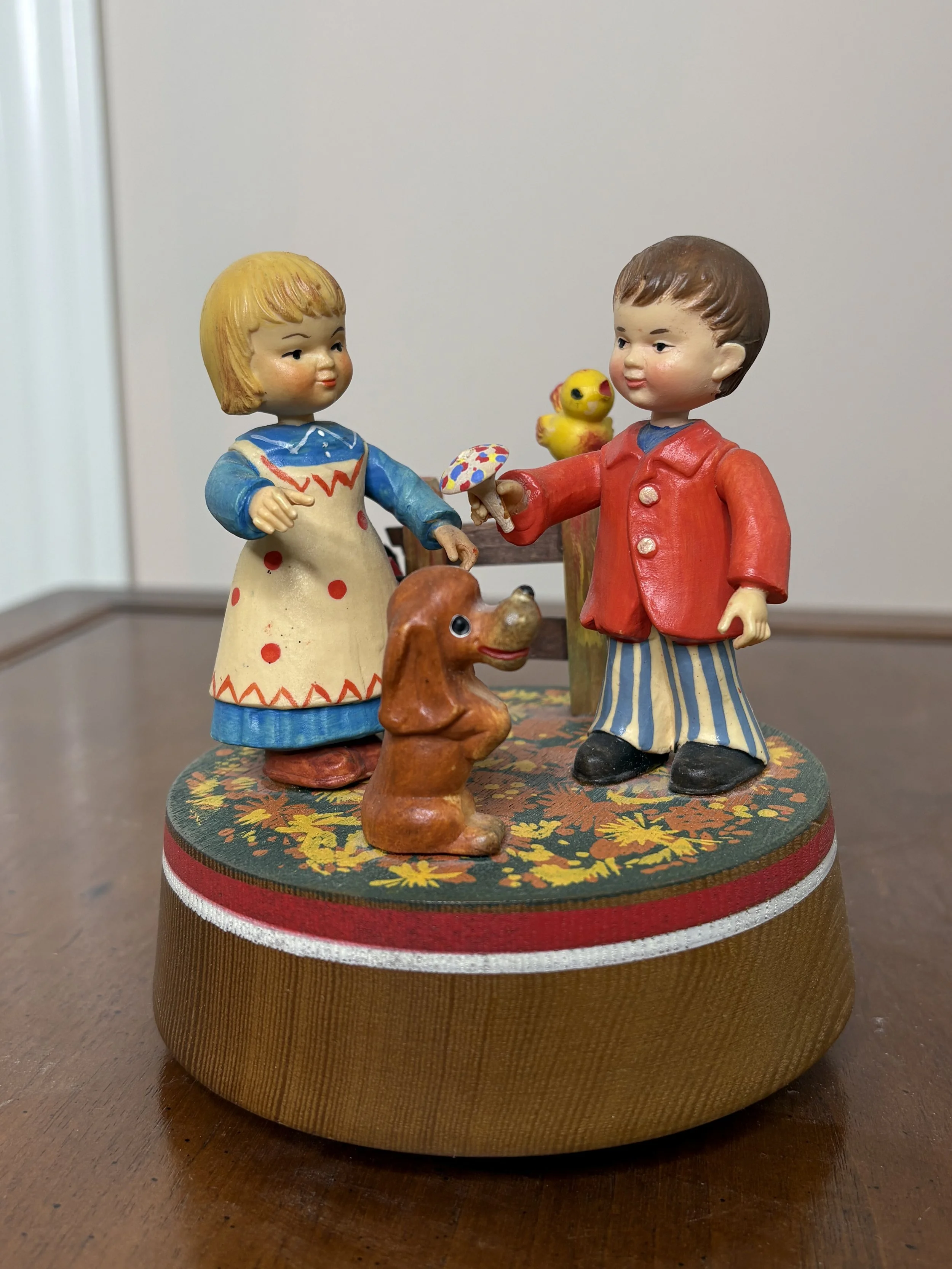 Vintage figurines of two children, a girl and a boy, with a dog and duck, on a round base with floral design.