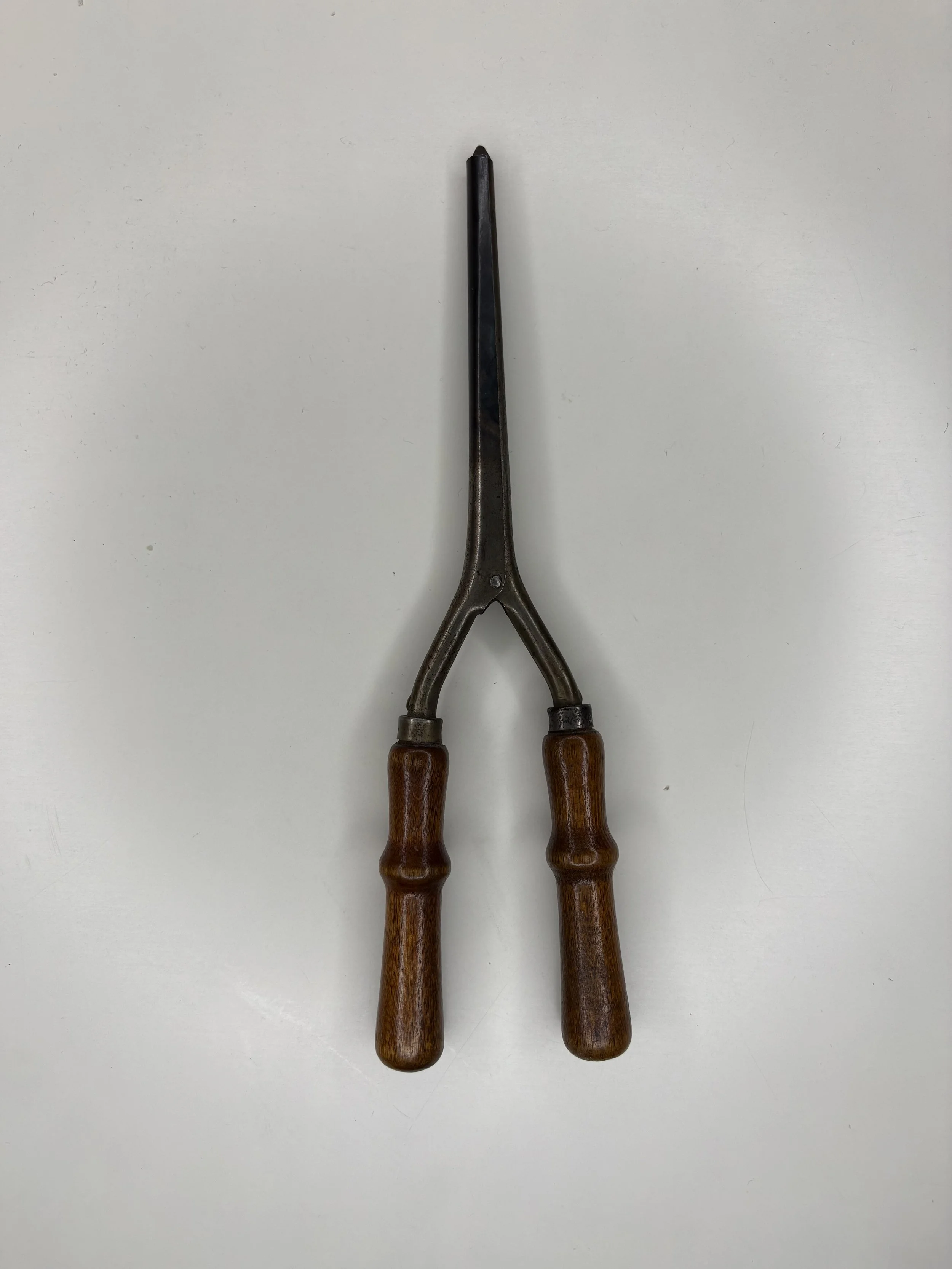 A pair of vintage tongs with wooden handles on a white surface.