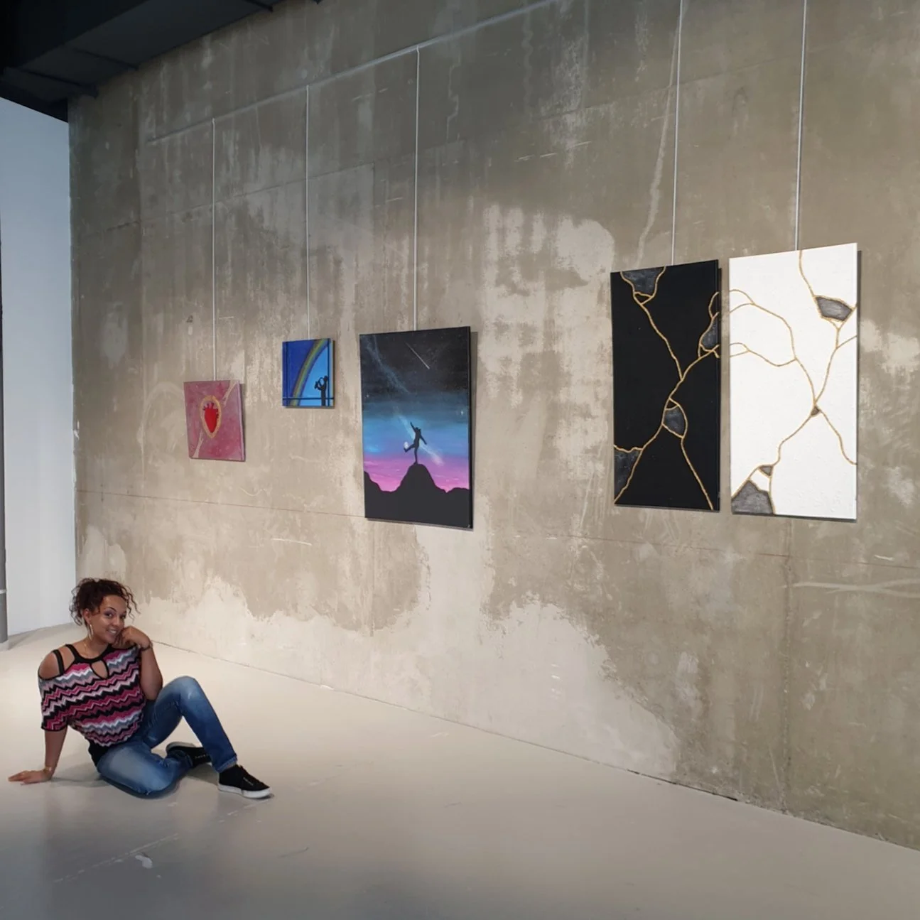 angélique assise sur le sol devant ses oeuvres exposées dans une gallerie