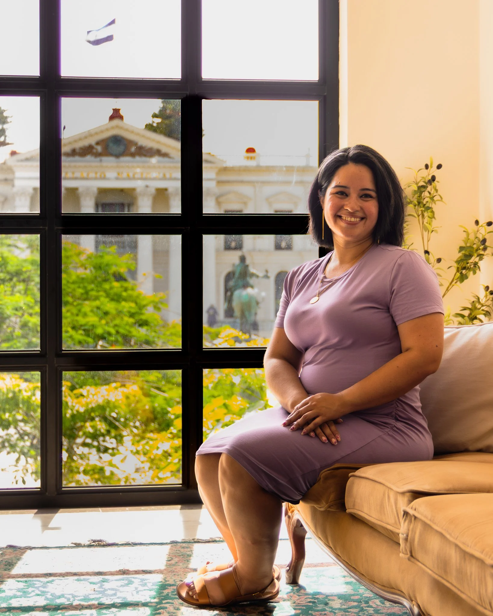 Geri Lopez, New Jersey trauma therapist for first generation women of color and queer adults, wearing a black jumpsuit smiling and leaning against a brick wall outside