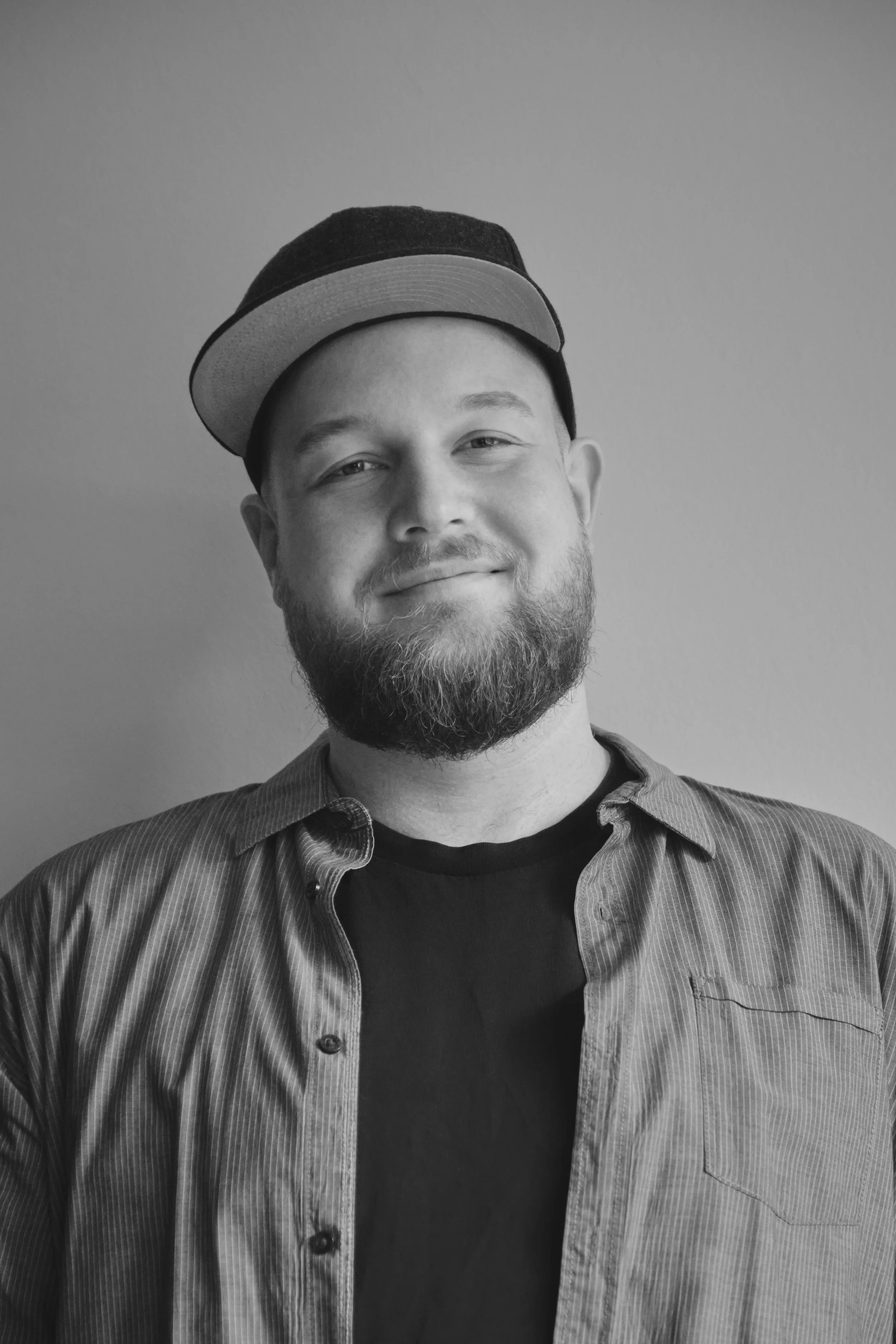 Schwarz weiß Portrait von FotoLukas. Er trägt eine Cap, ein graues Hemd und darunter ein schwarzes T-Shirt.