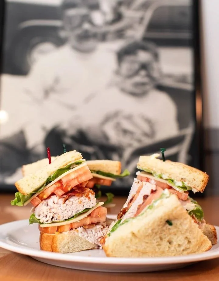 Sandwiches with sliced turkey, lettuce, tomato, and bread on a white plate, with a black and white photograph in the background.