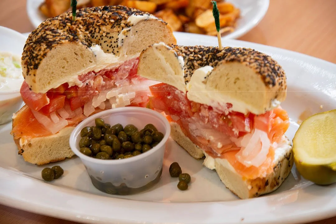 Bagel sandwich with smoked salmon, cream cheese, tomato, onions, and poppy seed crust, served with pickles and green peppercorns.