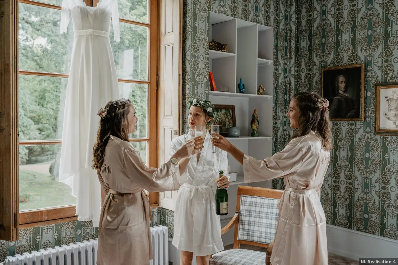 Trois femmes en peignoirs blancs célébrant avec des coupes de champagne dans une pièce décorée avec des bibelots et des portraits
