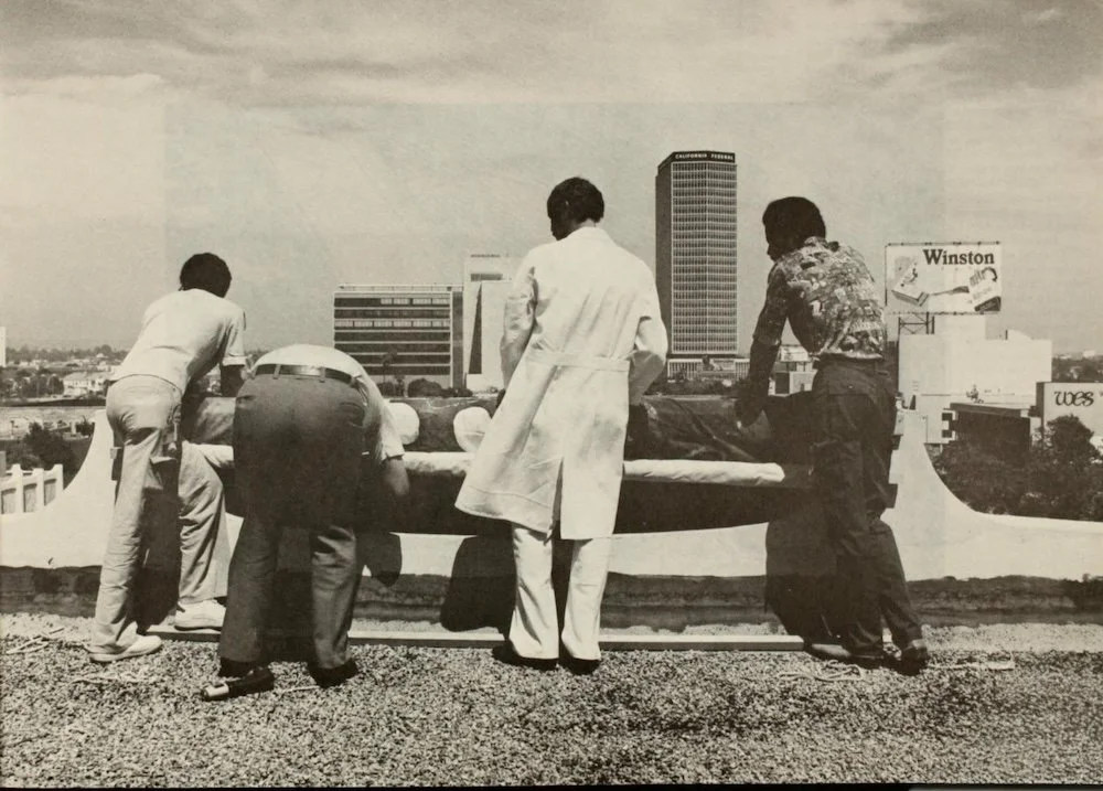 Five people on a rooftop leaning over the edge, looking at a body on a stretcher, with a city skyline in the background.