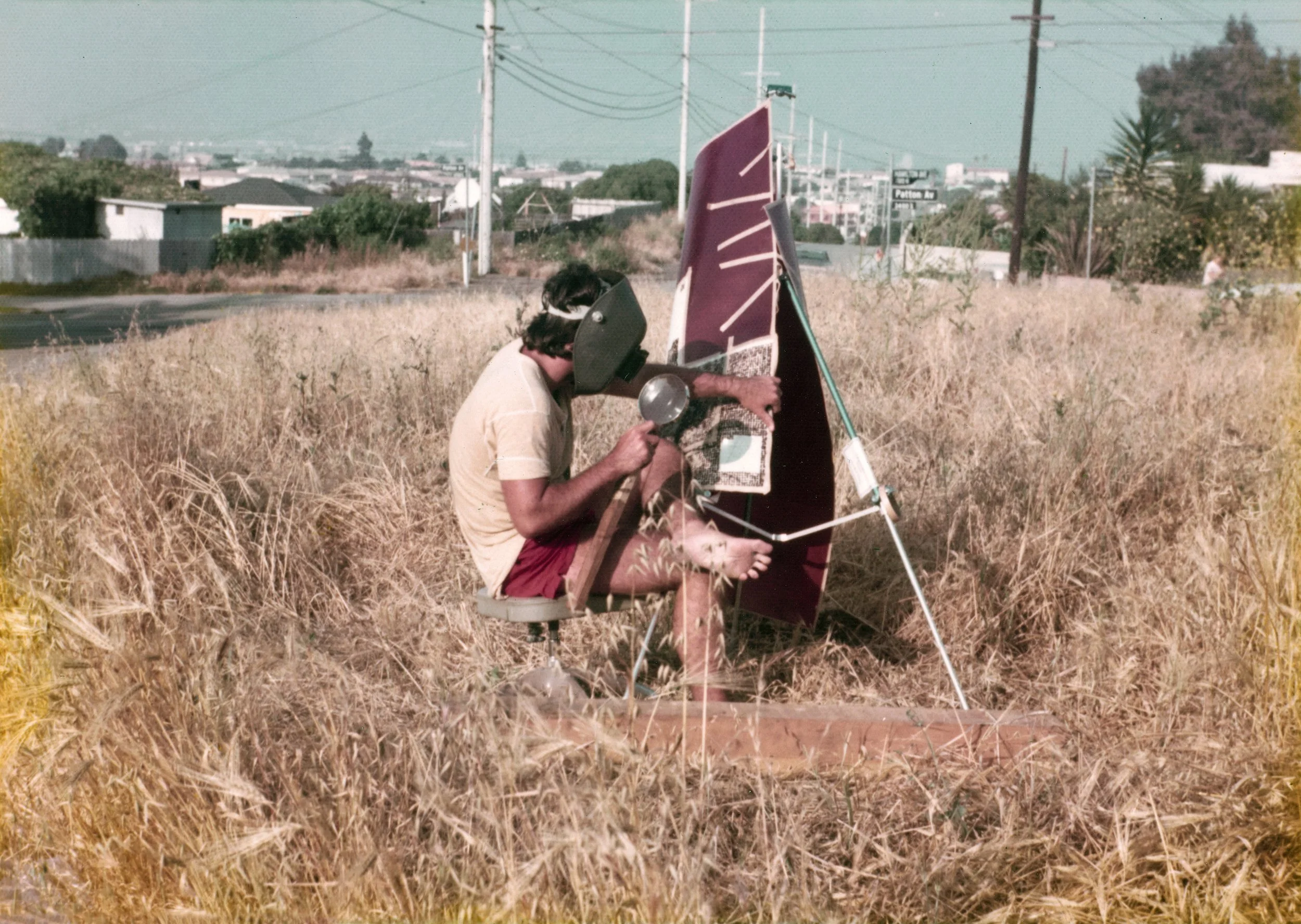 Person in a field with a mascara tube nearby, looking through a telescope at the sky.
