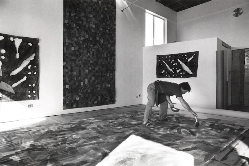 Person cleaning a large, abstract painting on the floor in an art gallery with artworks on the walls.