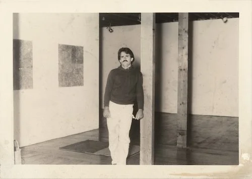 Black and white photo of a man standing in an art gallery or museum, with empty walls and wooden beams.