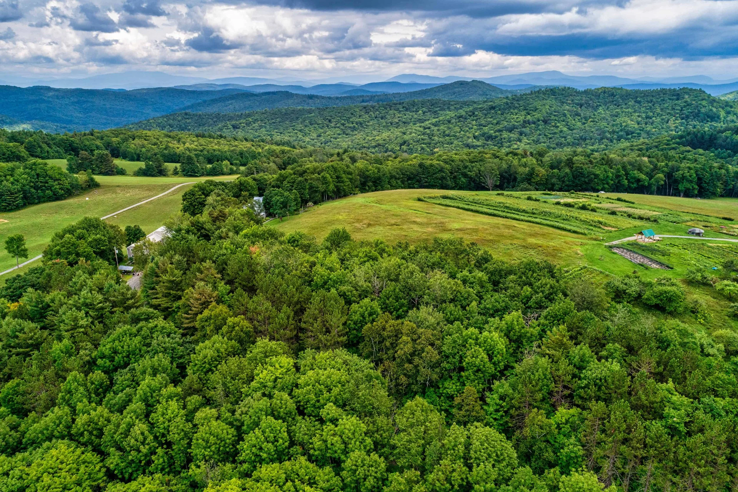 Aerial view of lush green mountains, fields, and a cloudy sky.