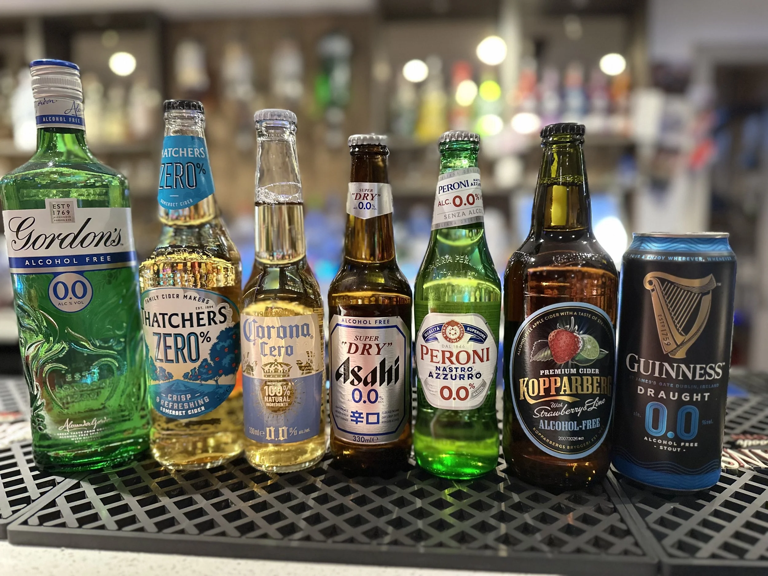 Lineup of alcohol-free beverages including Gordon's alcohol-free gin, Hatchers Zero cider, Corona Zero beer, Asahi alcohol-free beer, Peroni alcohol-free beer, Kopparberg strawberry and lime cider, and Guinness alcohol-free stout, arranged on a black