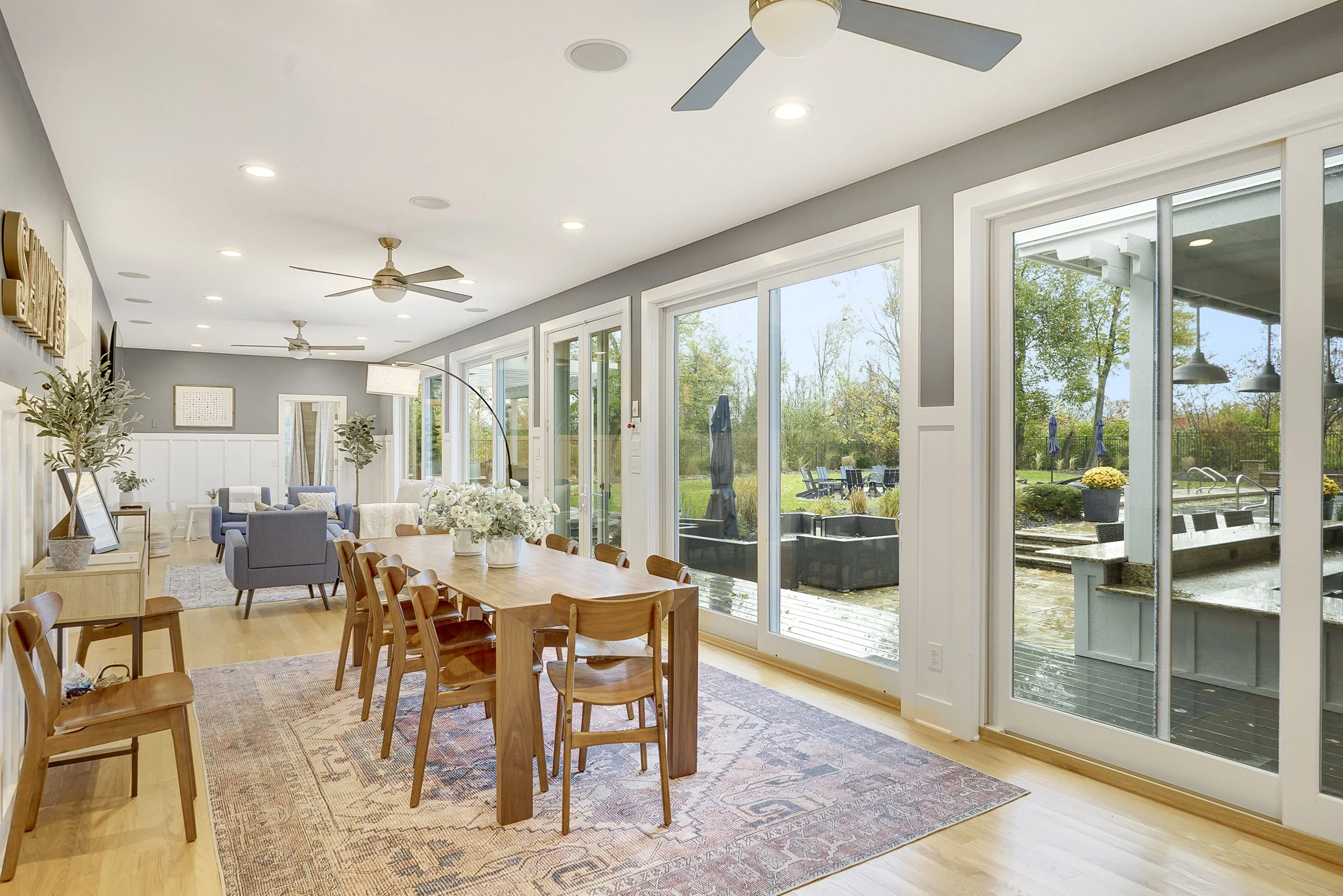 Bright open living and dining room with large sliding glass doors overlooking a backyard with trees, patio furniture, and an outdoor hot tub.