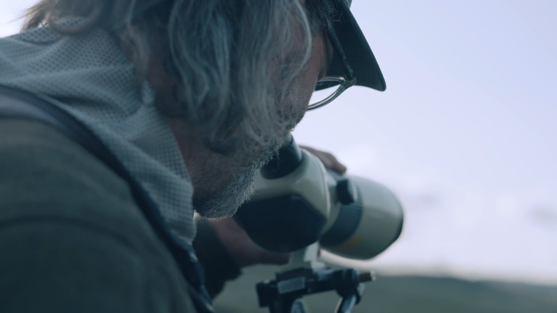 A man with gray hair and glasses looking through a telescope outdoors.