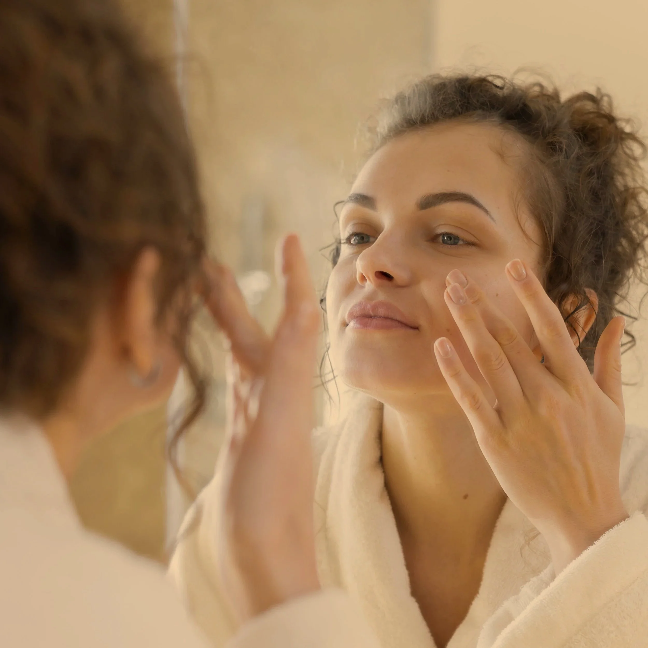 A woman looking in the mirror and applying skincare to her face.