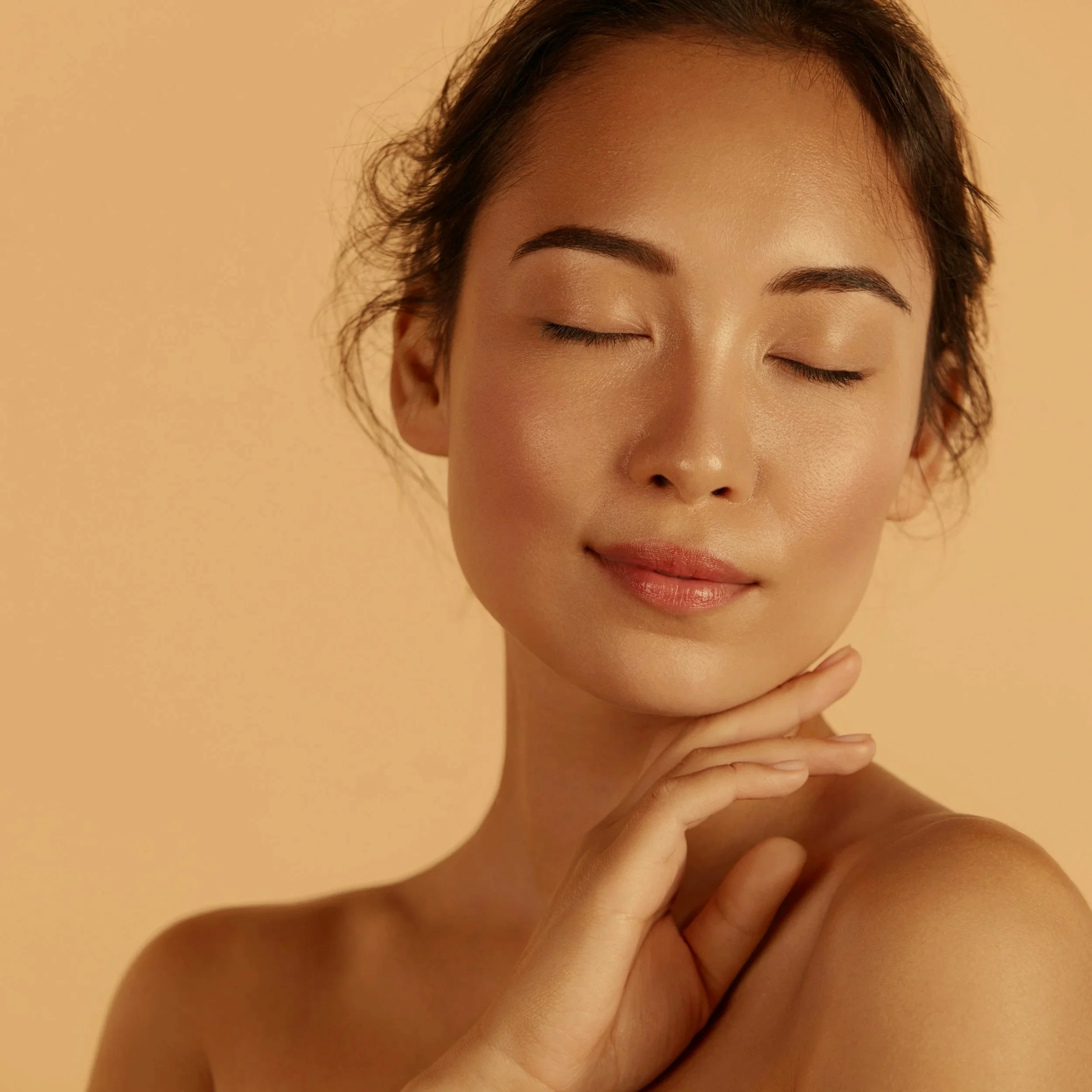 Close-up portrait of a woman with her eyes closed and a gentle smile, touching her chin with her hand.