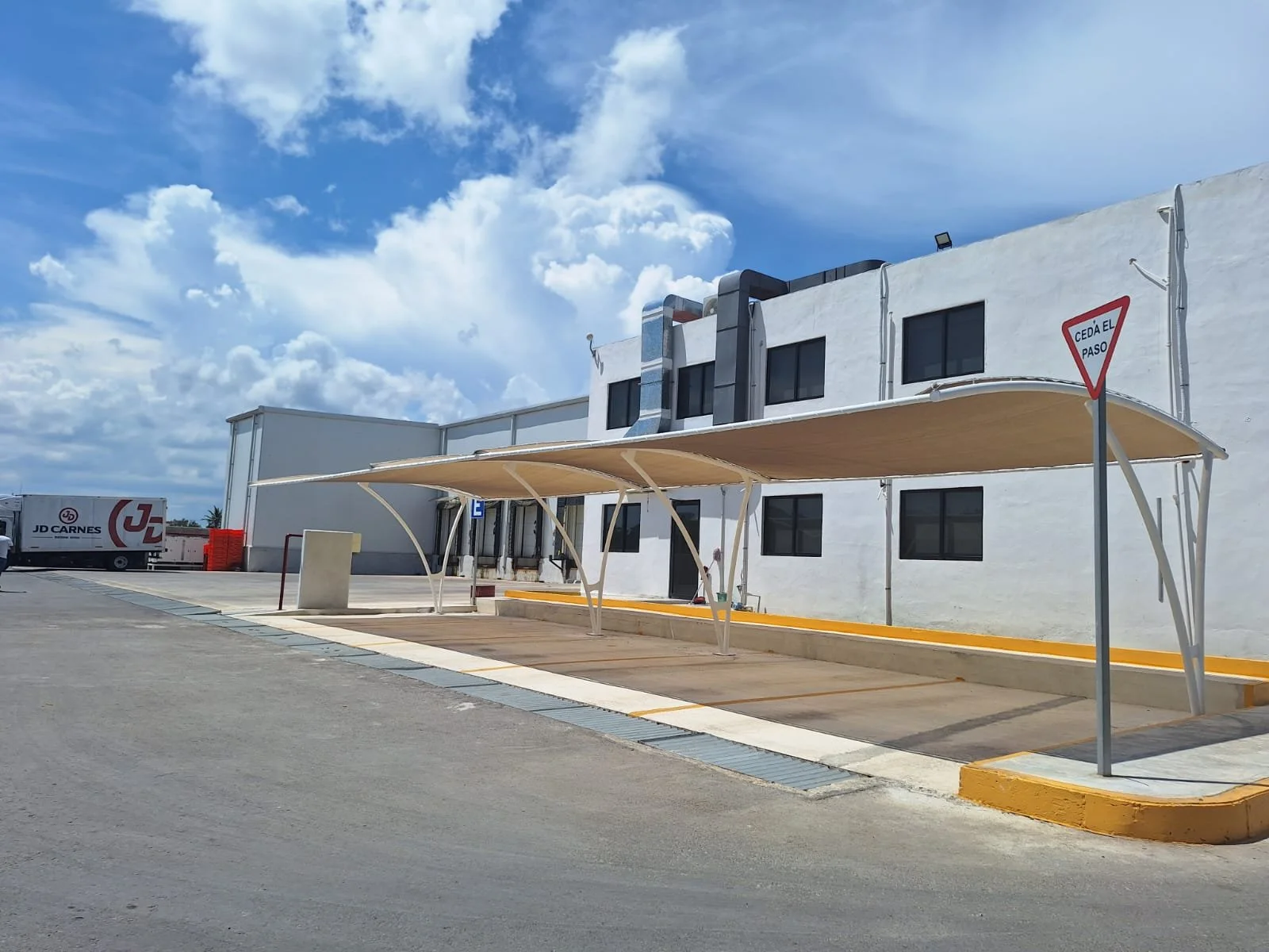 Malla sombra tensada sobre estacionamiento en edificio comercial, estructura de protección exterior por Seaak Outdoor en Cancún.