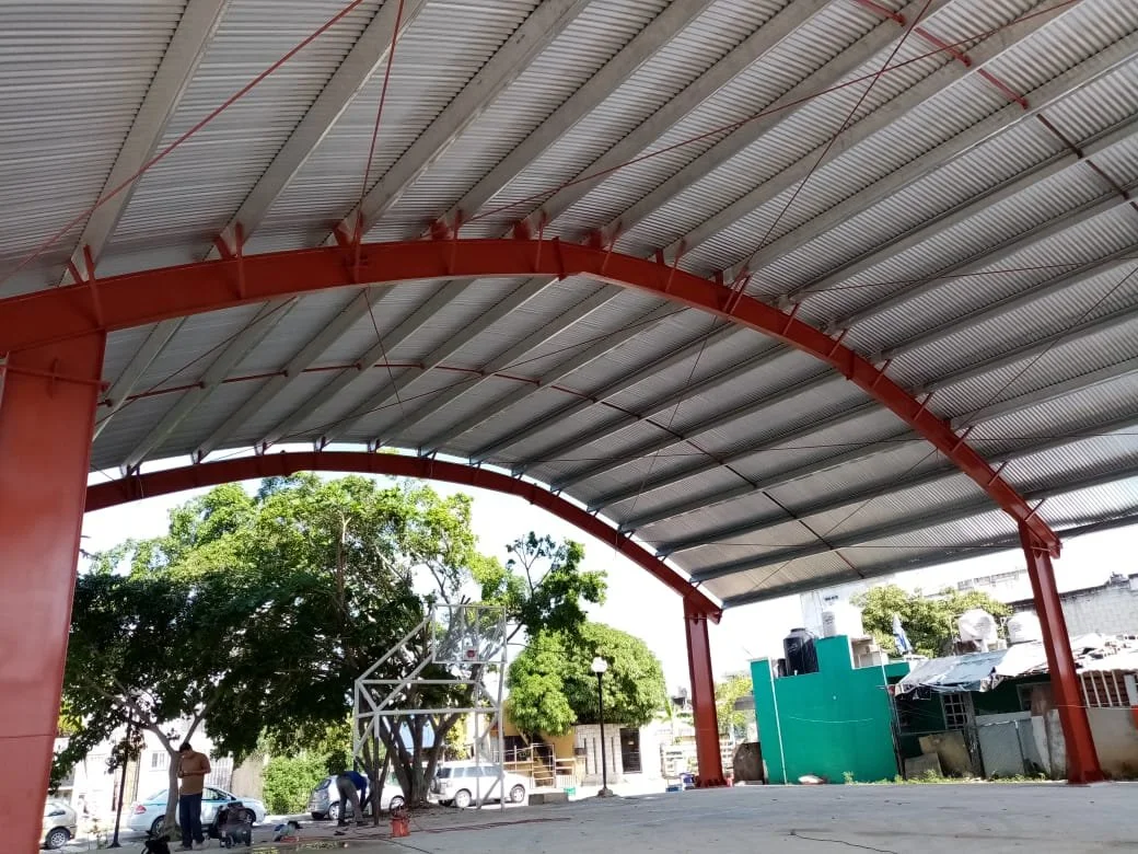 Domo de estructura metálica con arcos de acero rojo y lámina galvanizada sobre cancha deportiva en Cancún, por Seaak BS.