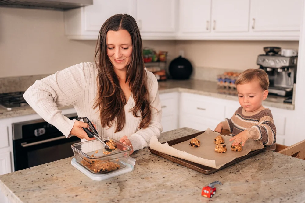 Mom scooping cookie dough as their toddler places dough balls on the tray