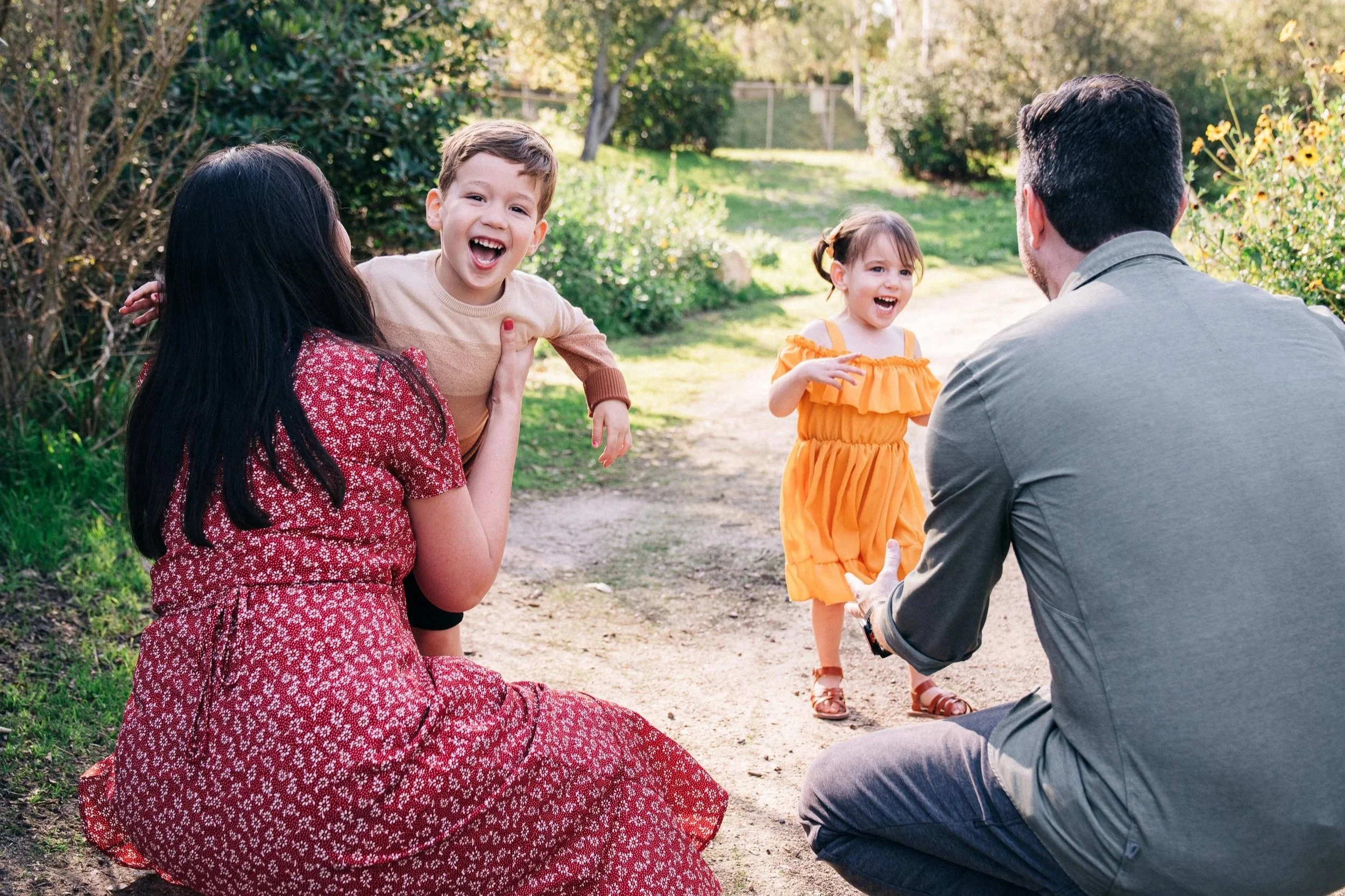 A family enjoying time outdoors in a park, with two children and two adults, all smiling and interacting in a sunny setting.