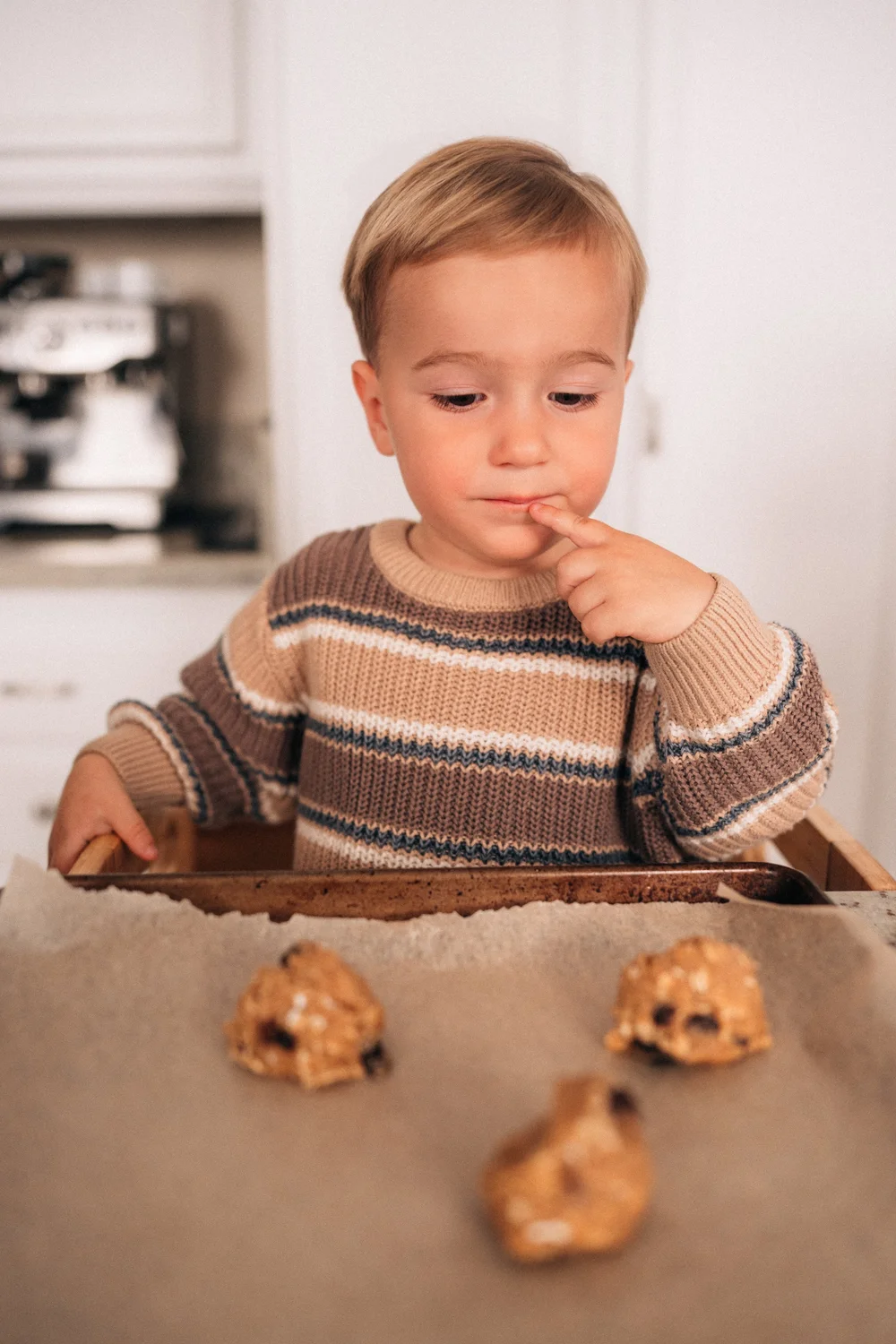 Toddler tasting cookie dough off his finger, sweet and serious